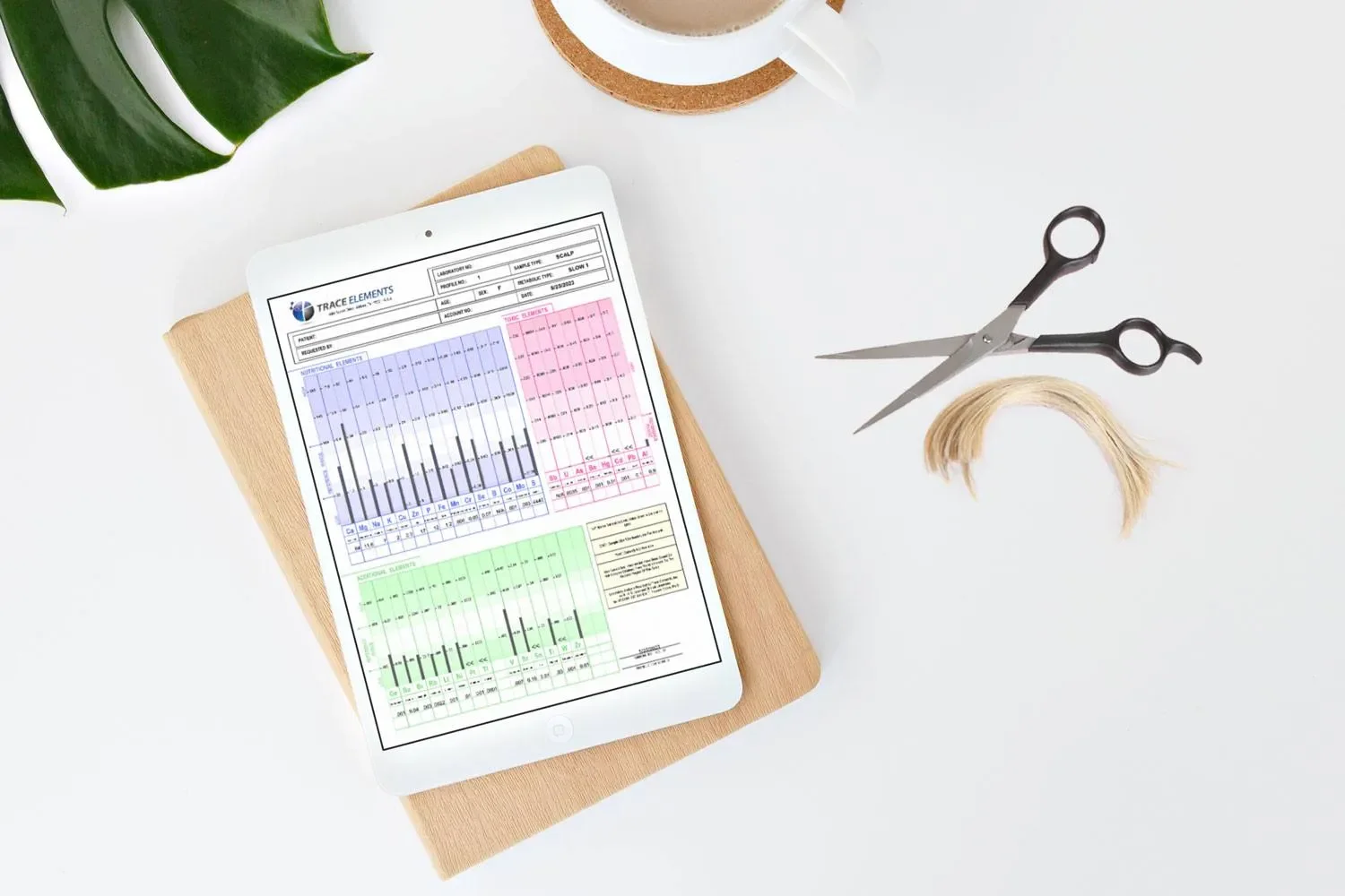 A tablet with a chart on a notebook, scissors, a lock of hair, a cup of coffee, and a green leaf on a white surface.