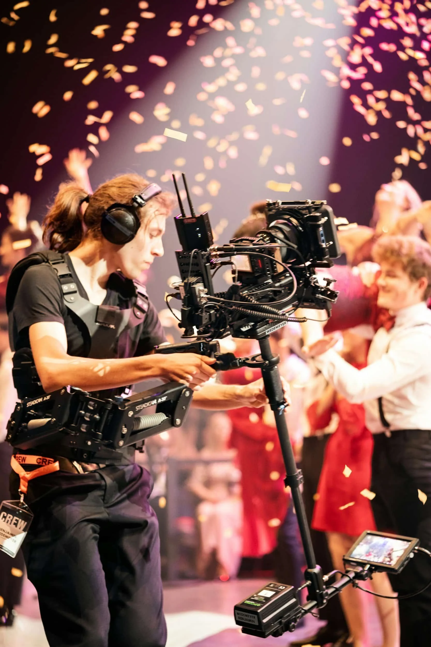A camera operator films a lively party scene with confetti falling and people dancing in the background.