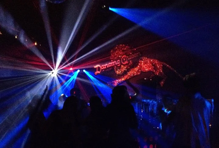 People dancing in a dark nightclub with colorful laser lights and a sign that reads Dancing Onion above a glowing lion figure.