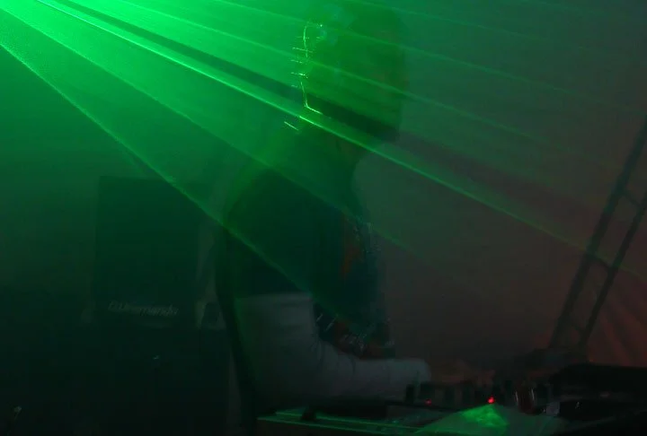 A DJ performing in dim lighting with green laser lights beaming across the scene, creating a vibrant party atmosphere.