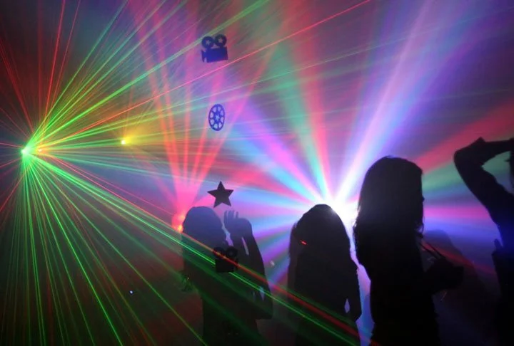 Silhouettes of people dancing amid colorful laser lights and fog at a lively party or nightclub