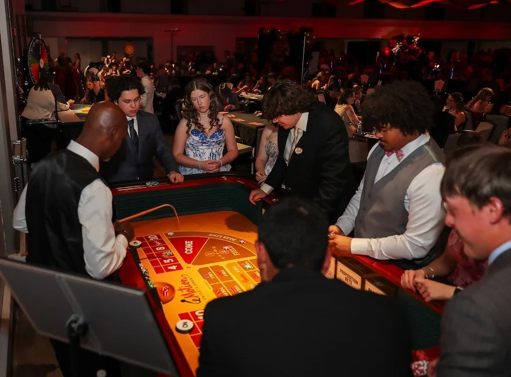 A group of young people in formal wear enjoy a casino table game at a lively casino rental event.