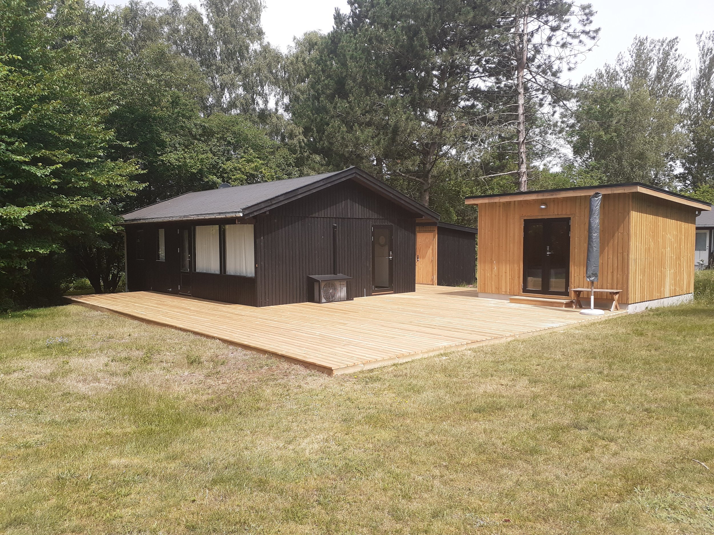 Moderne bolig med træterrasse omgivet af grøn natur.