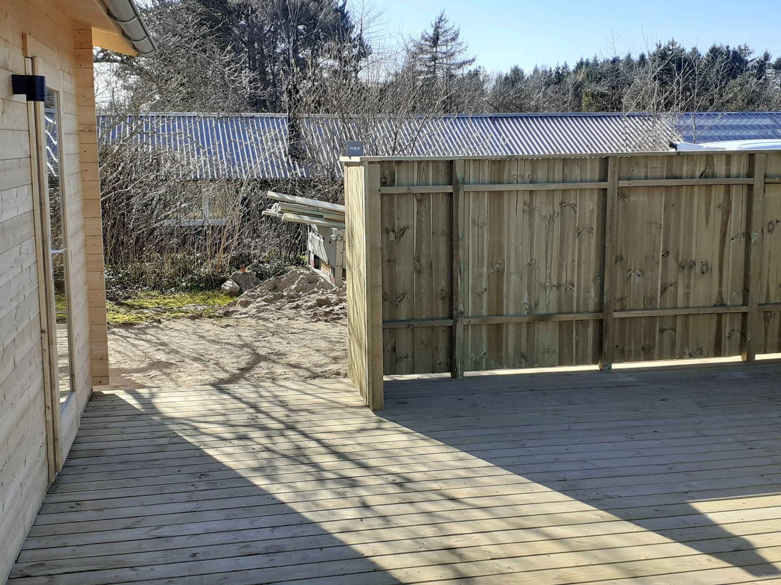 Træterrasse i baghave med nyt hegn. Det gamle hegn ses delvist i baggrunden sammen med nabohuse og træer.