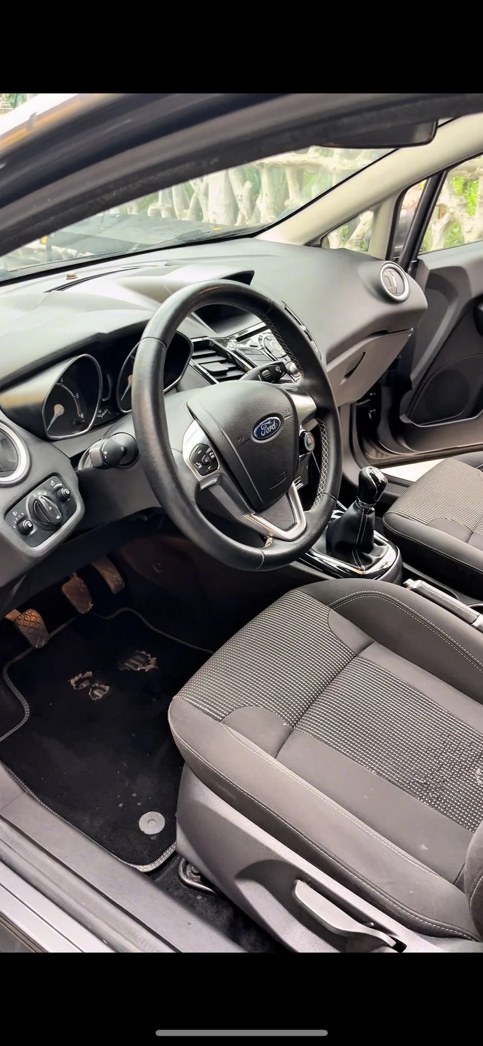 Interno di un'auto con volante, cambio manual e sedili in tessuto, pannello strumenti e comandi