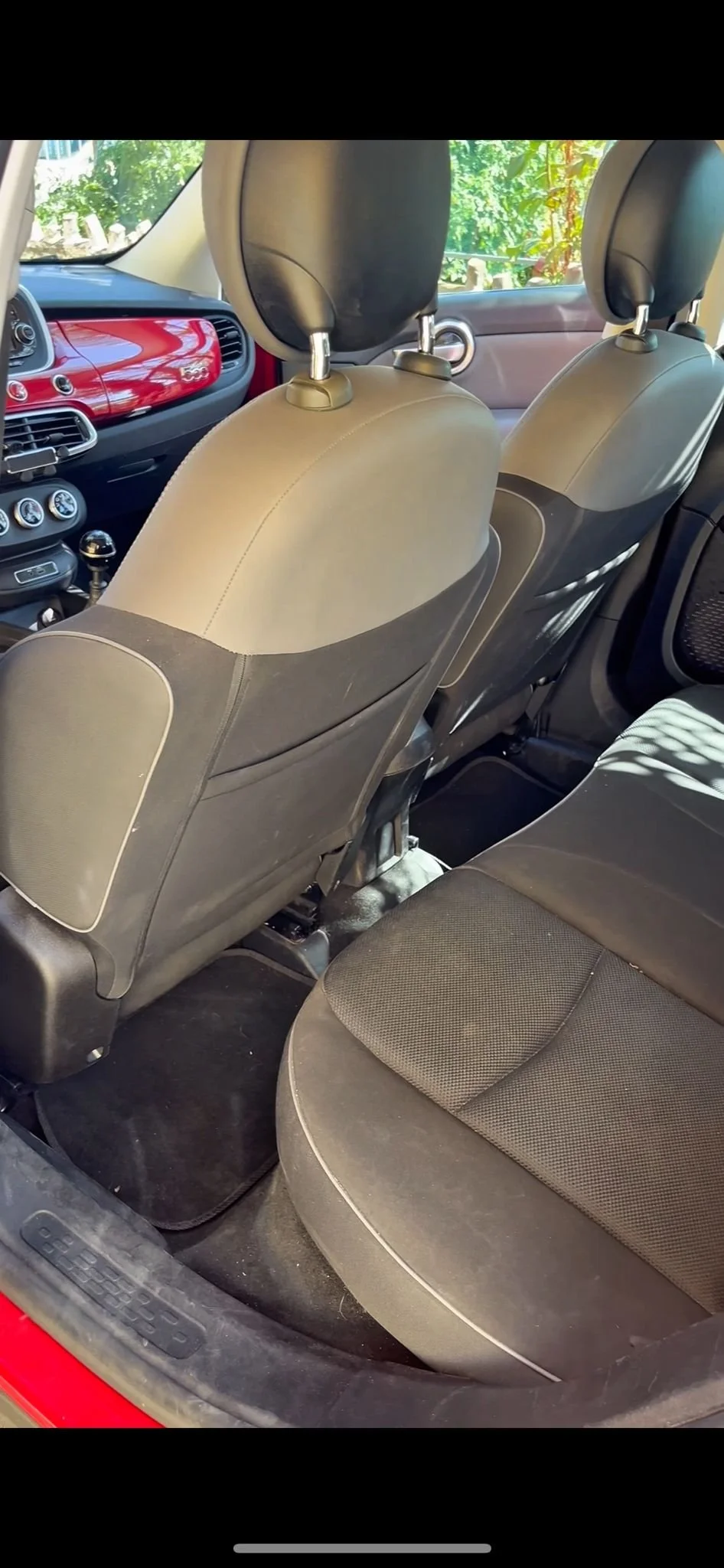 Interno di un'auto con sedili in tessuto scuro e cruscotto rosso, vista dal posteriore con i sedili anteriori visibili