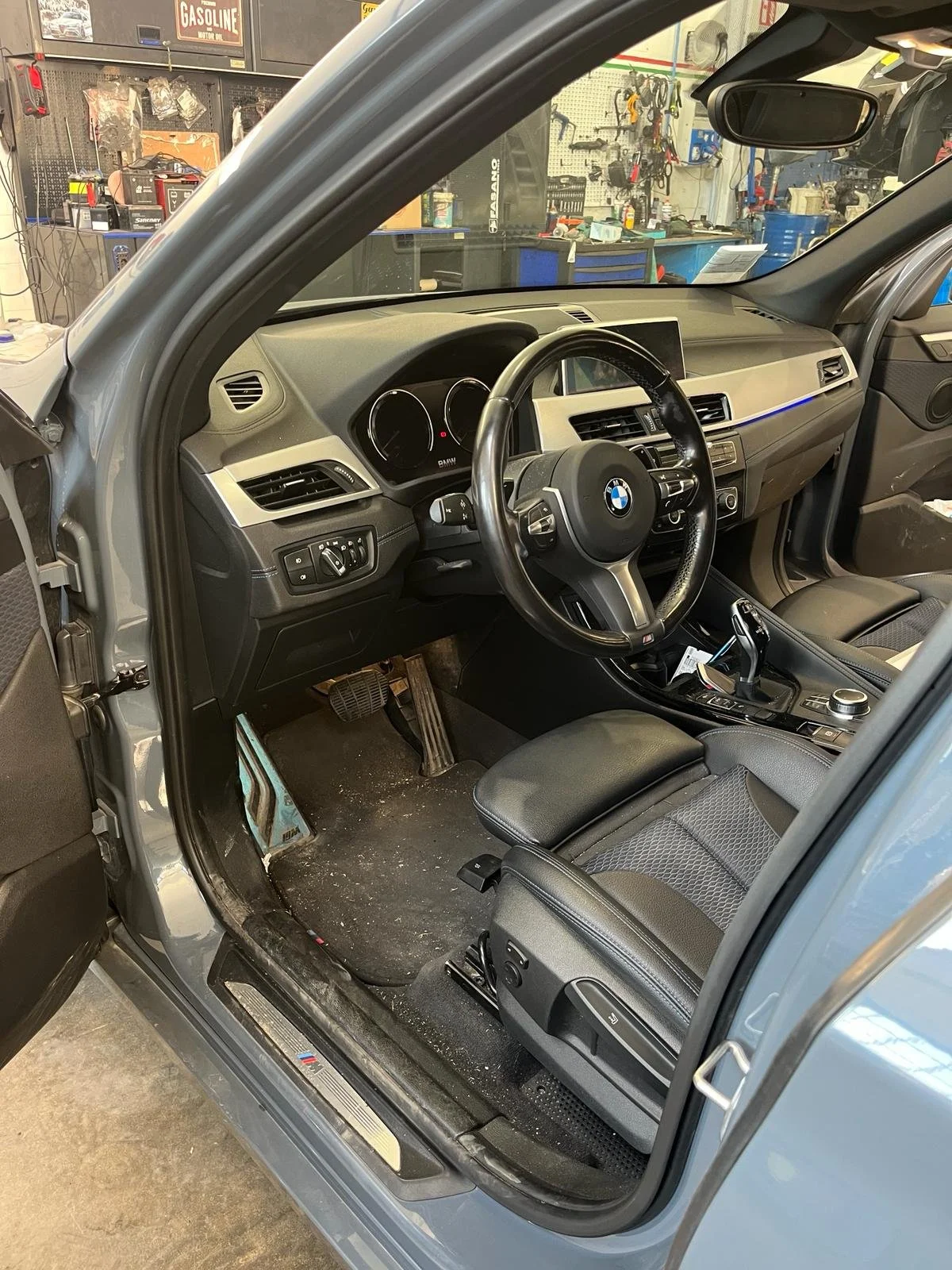 Interno di un'auto BMW in un'officina, con volante, cruscotto e sedile.