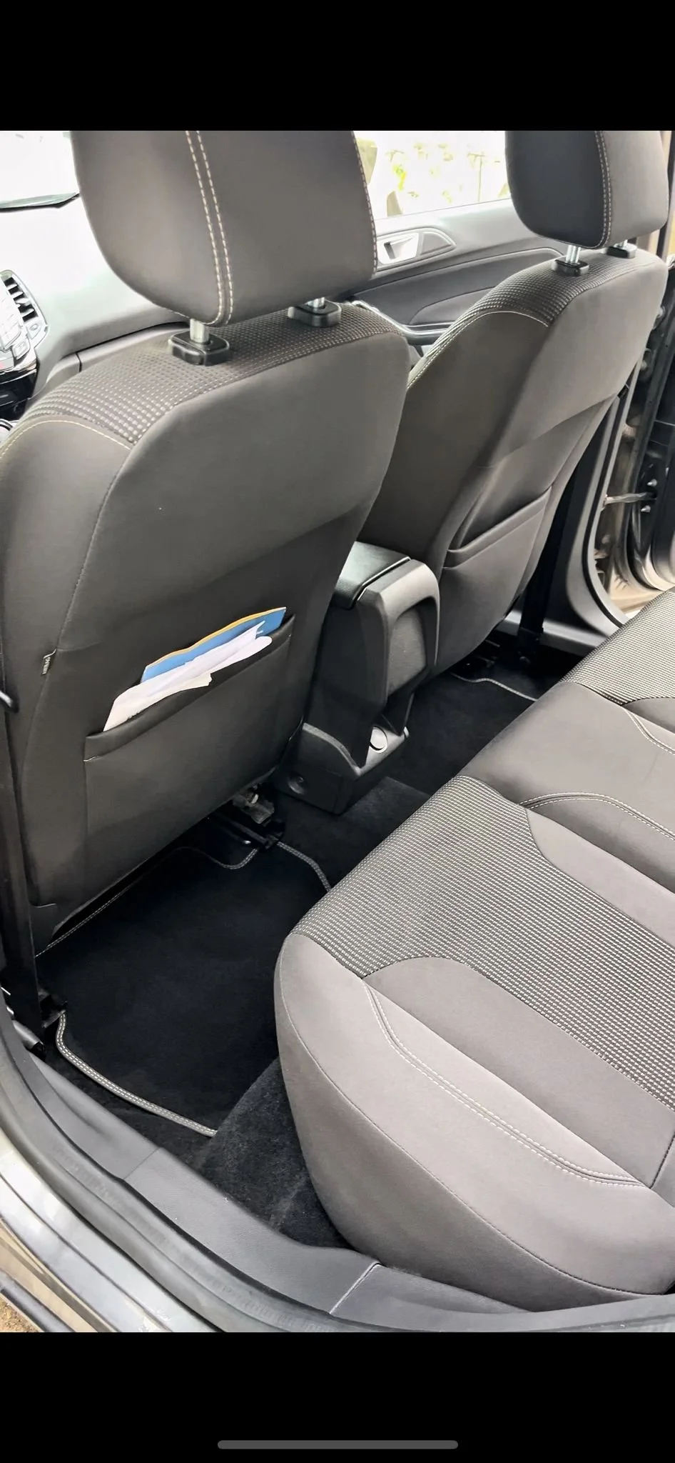 Interno di un'auto con sedili in tessuto nero e tappeti neri, vista della parte posteriore e dei sedili anteriori.