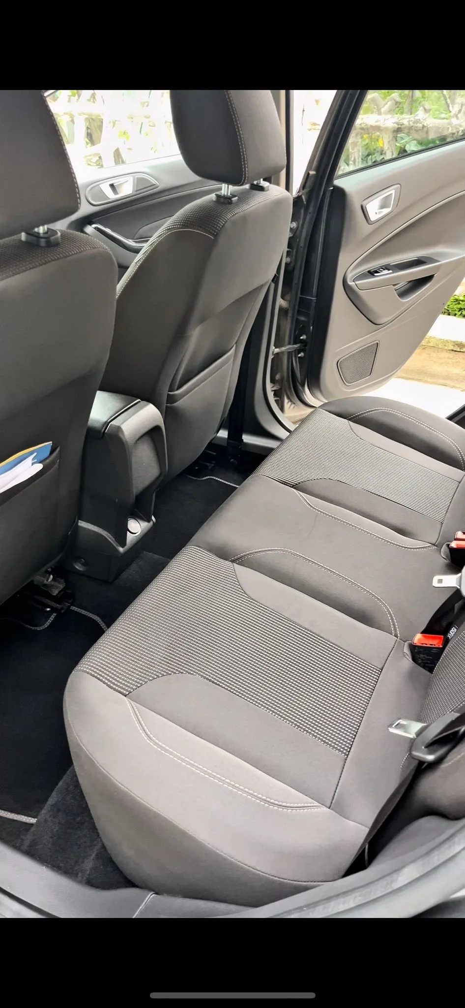 Interno di un'auto, vista sui sedili posteriori e parte delle portiere, con sedili in tessuto grigio e dettagli di cuciture bianche.