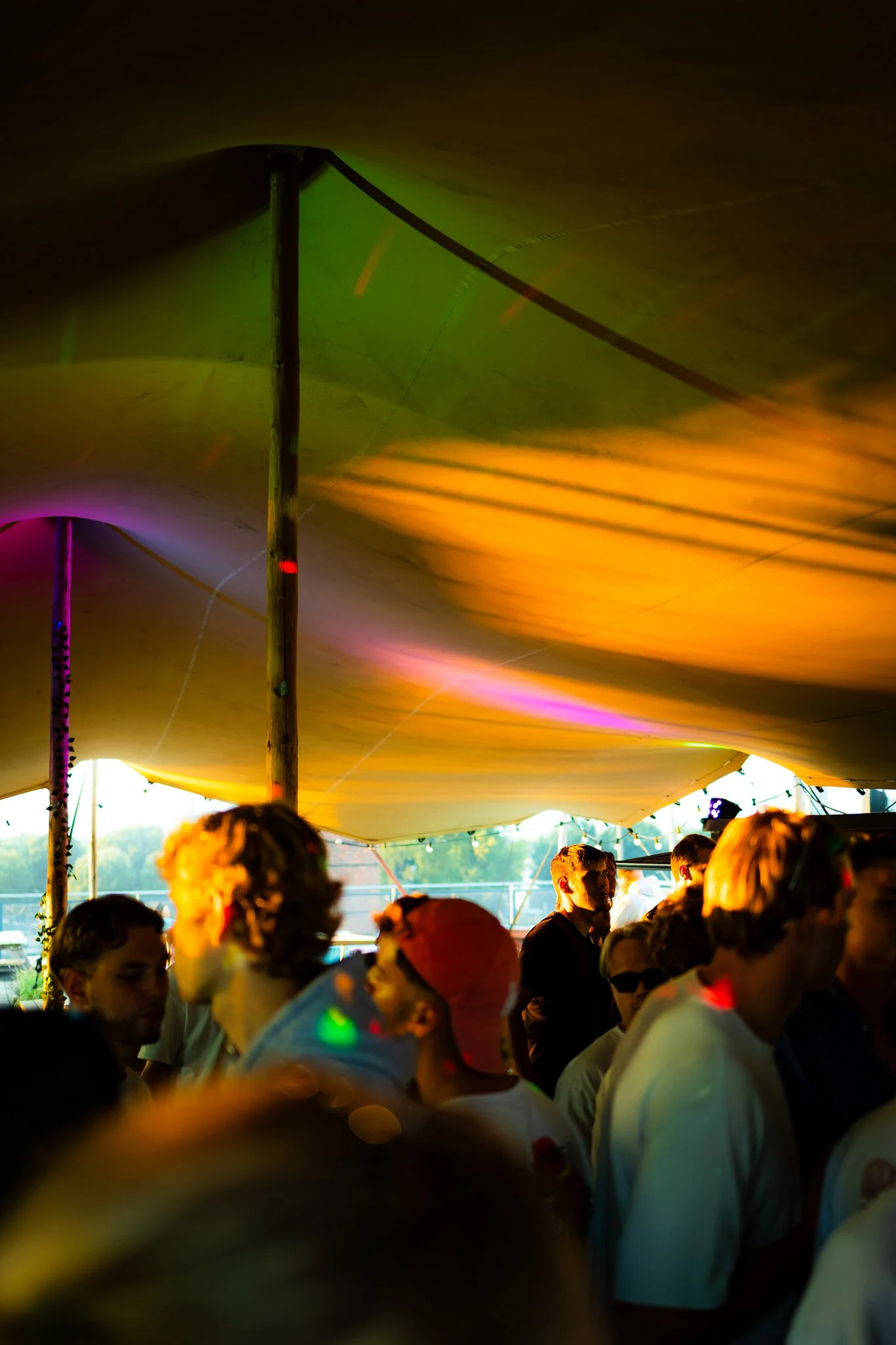 A crowd of people under a tent with colorful lighting at an outdoor event.