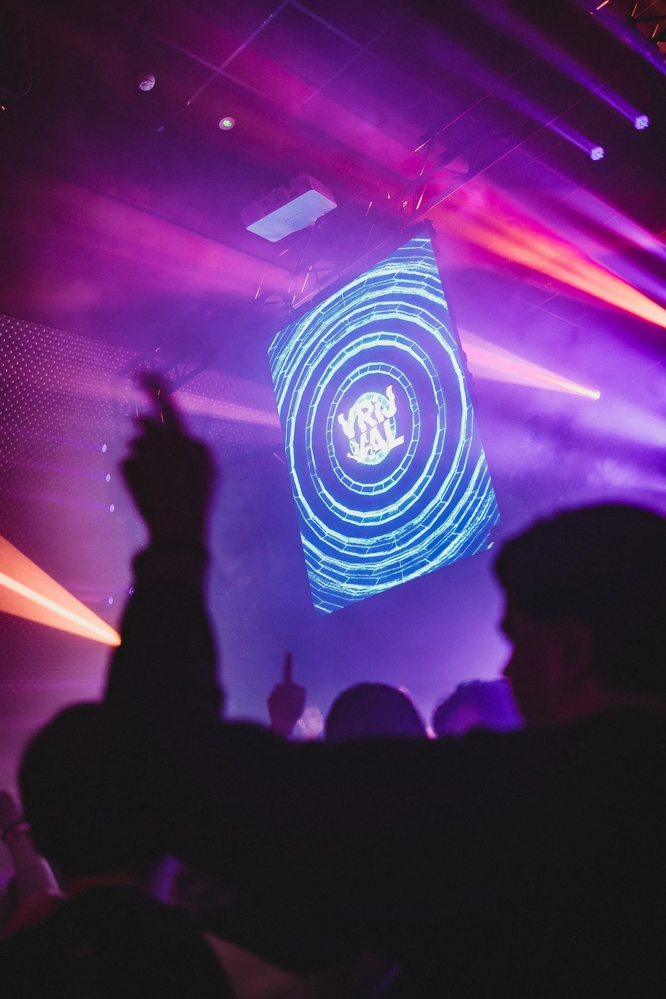 People dancing at a club or concert with colorful lights and a large digital screen displaying the word 'VIRAL' in the background.