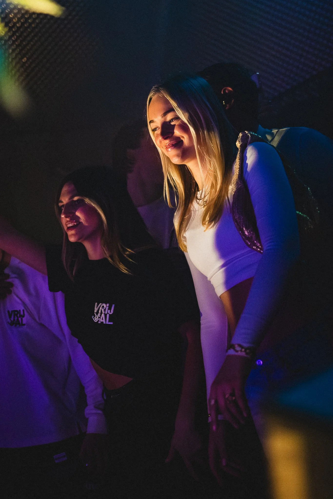 Two young women dancing in a club with colorful lighting.