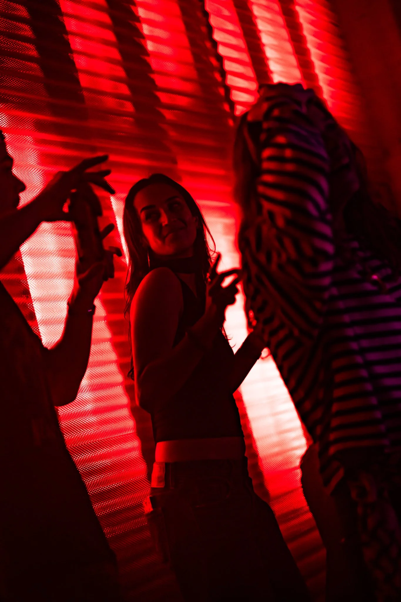 Silhouettes of people dancing in front of a red-lit outdoor wall, with one woman smiling.