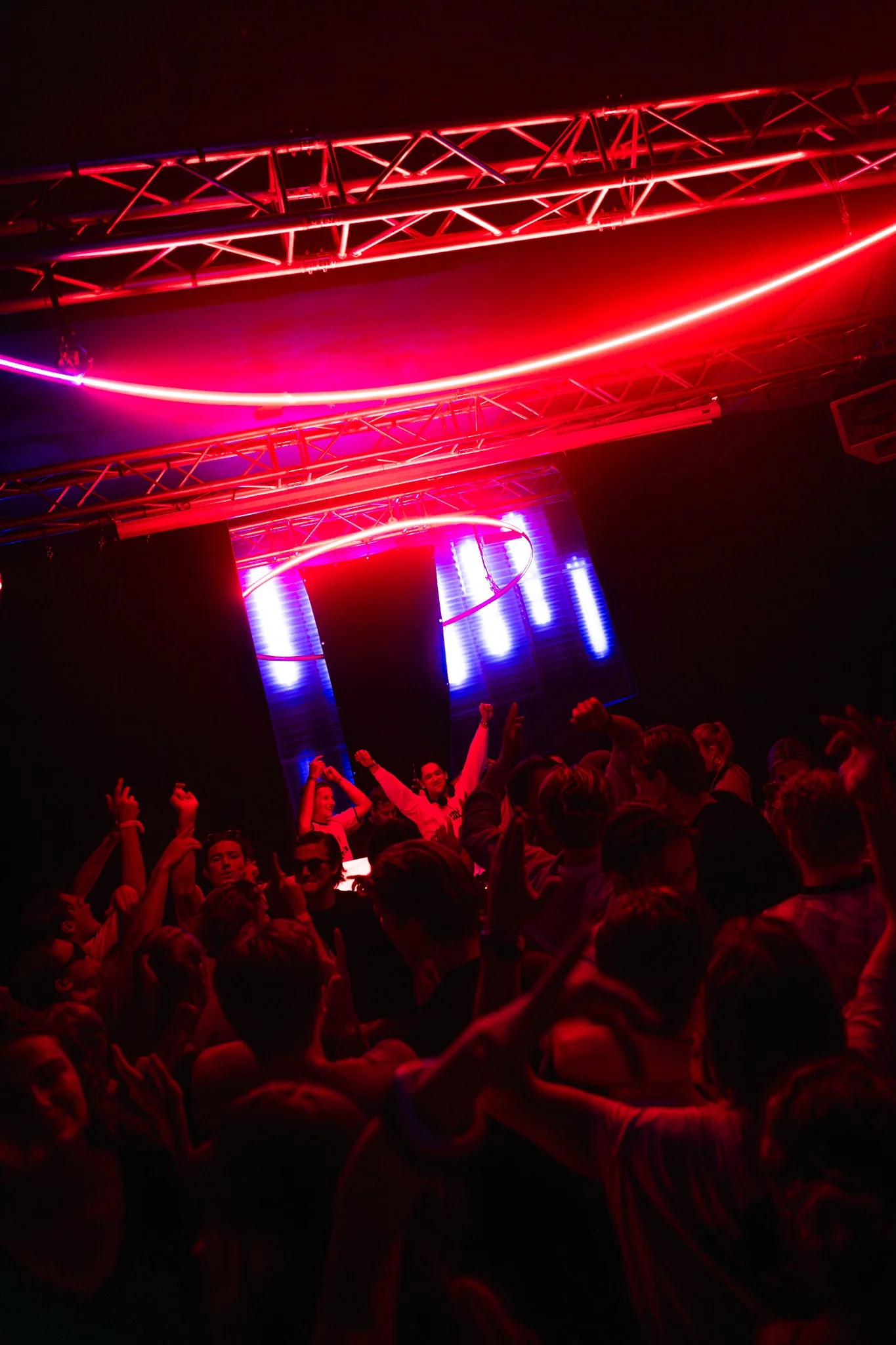 Crowd of people dancing and enjoying at a nightclub with vibrant neon red and blue lights.
