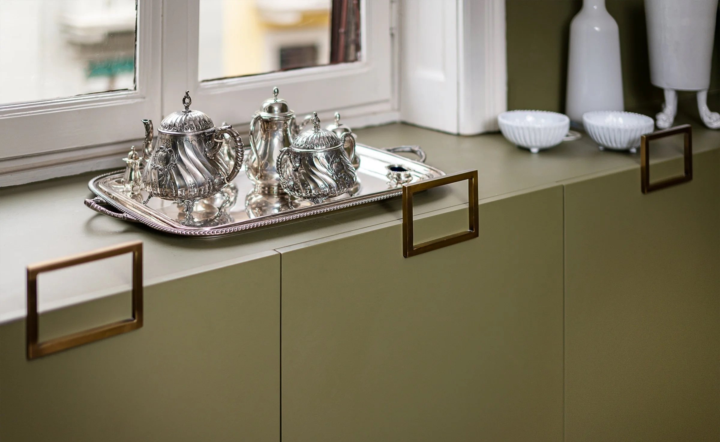 Vetrina con servizi in argento, due ciotole bianche e contenitori decorativi in ceramica su un mobile verde