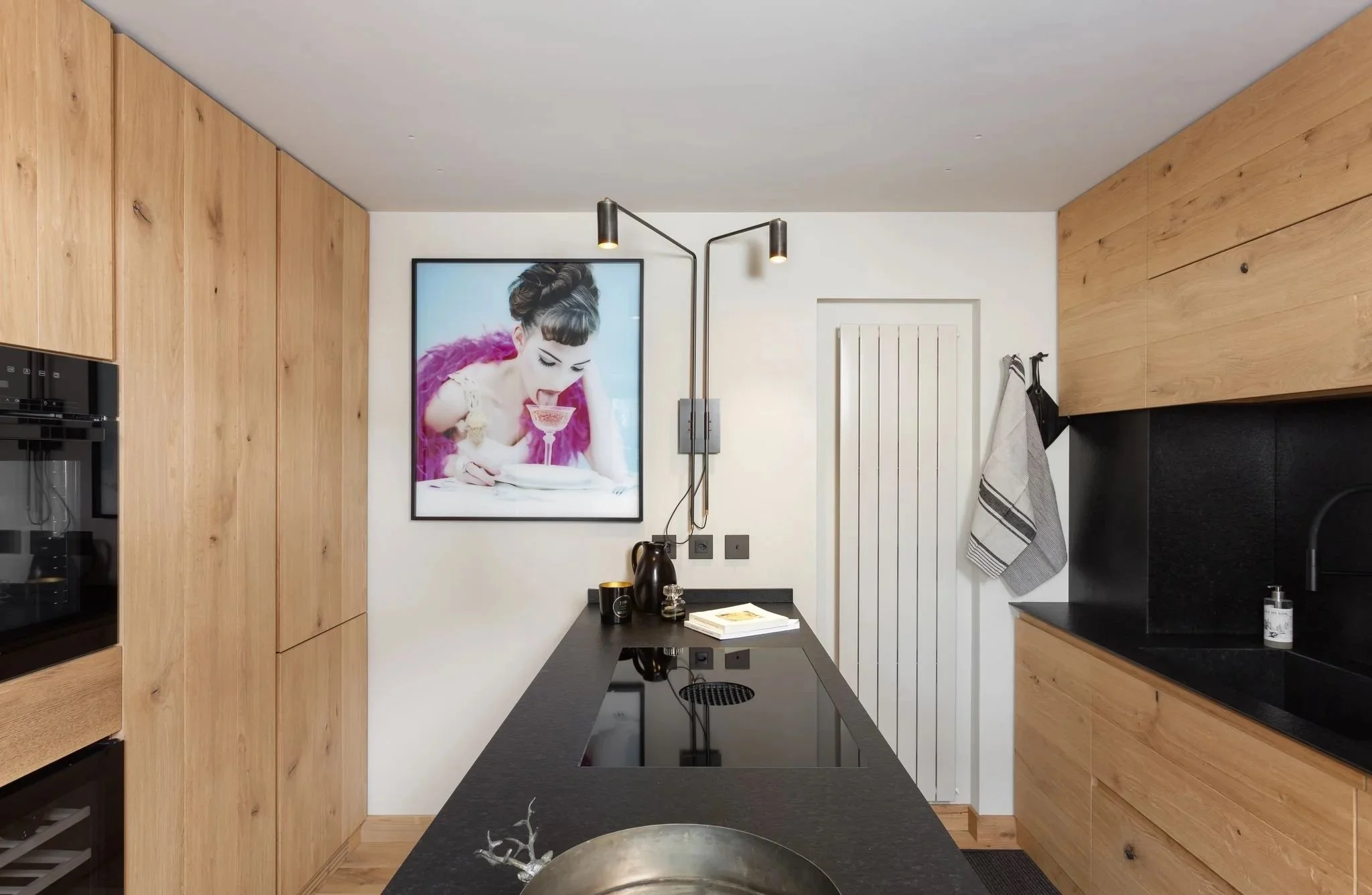Cucina moderna con pareti di legno e piani di lavoro neri, grande quadro di donna con cappello, illuminazione a parete