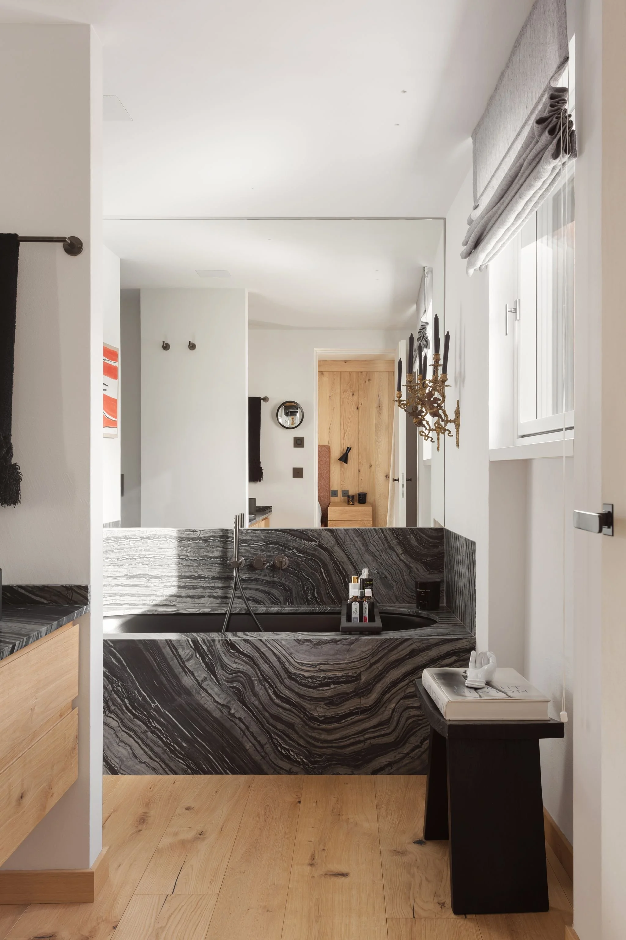 Interno di un bagno con pareti bianche, vasca da bagno in marmo scuro con venature nere e grigie, e un pavimento in legno chiaro