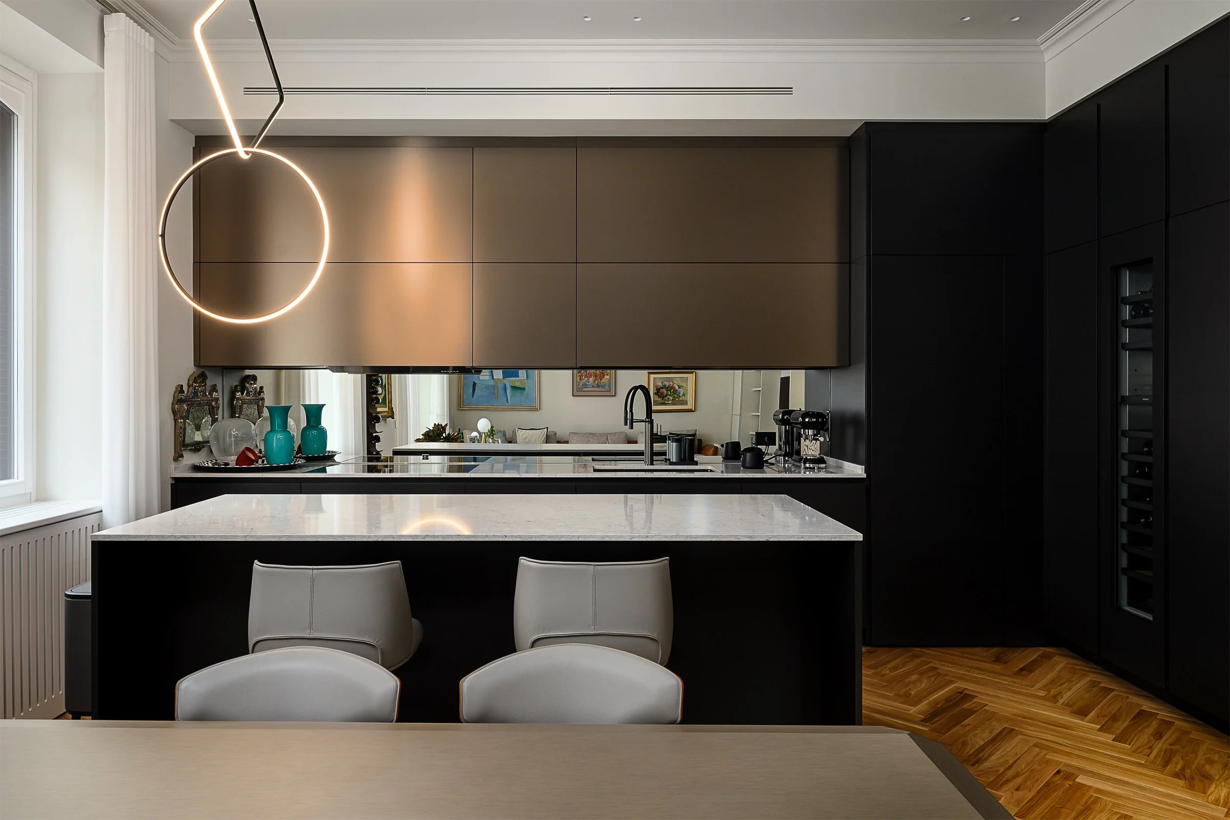 Cucina moderna con isola centrale, sedie beige, mobili neri, pareti nere, parete con tappi di vino, decorazioni con vasi blu e quadri alle pareti