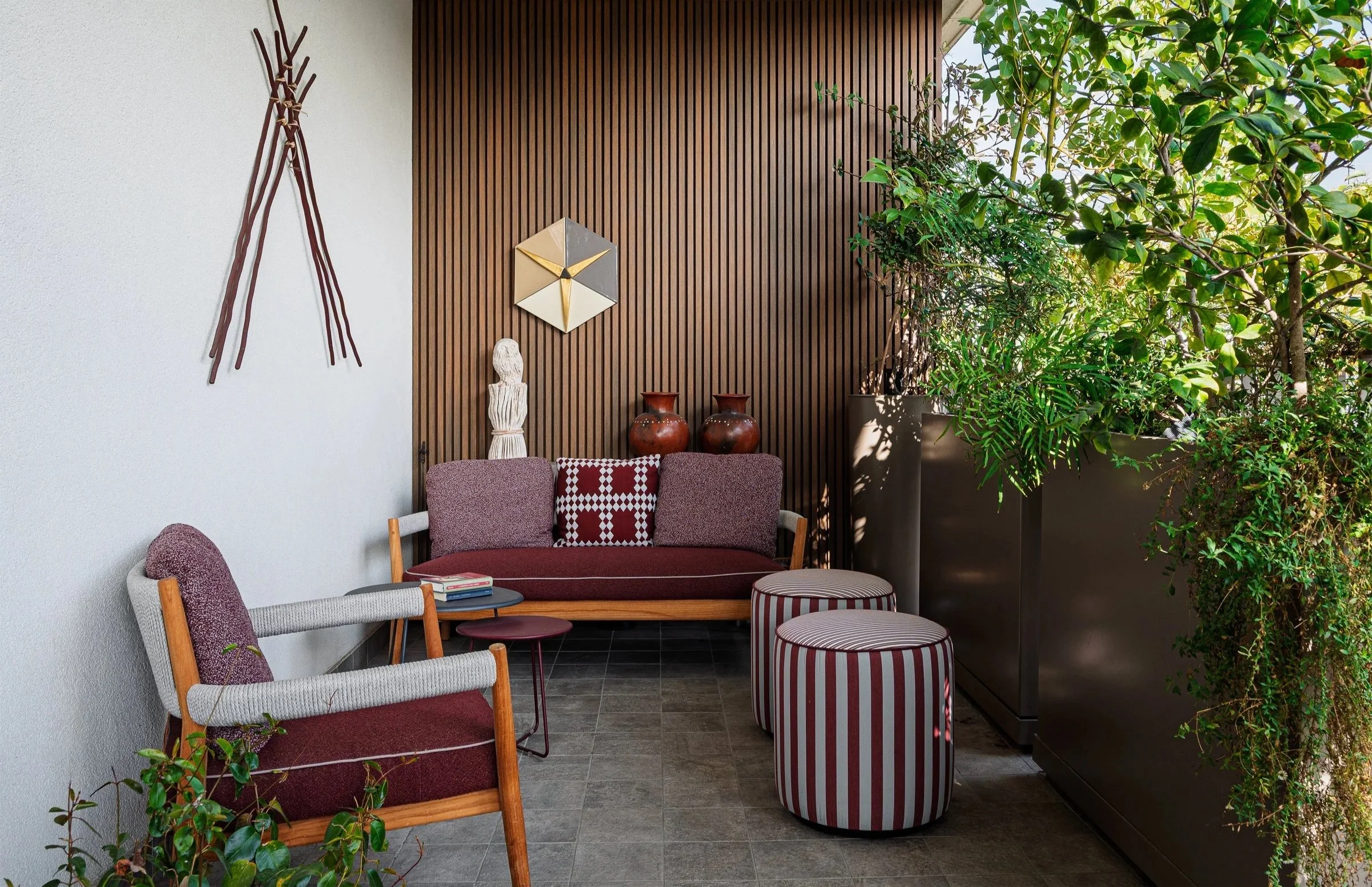 Spazio esterno arredato con sedie, poltrone, piante alte e decorazioni artistiche.