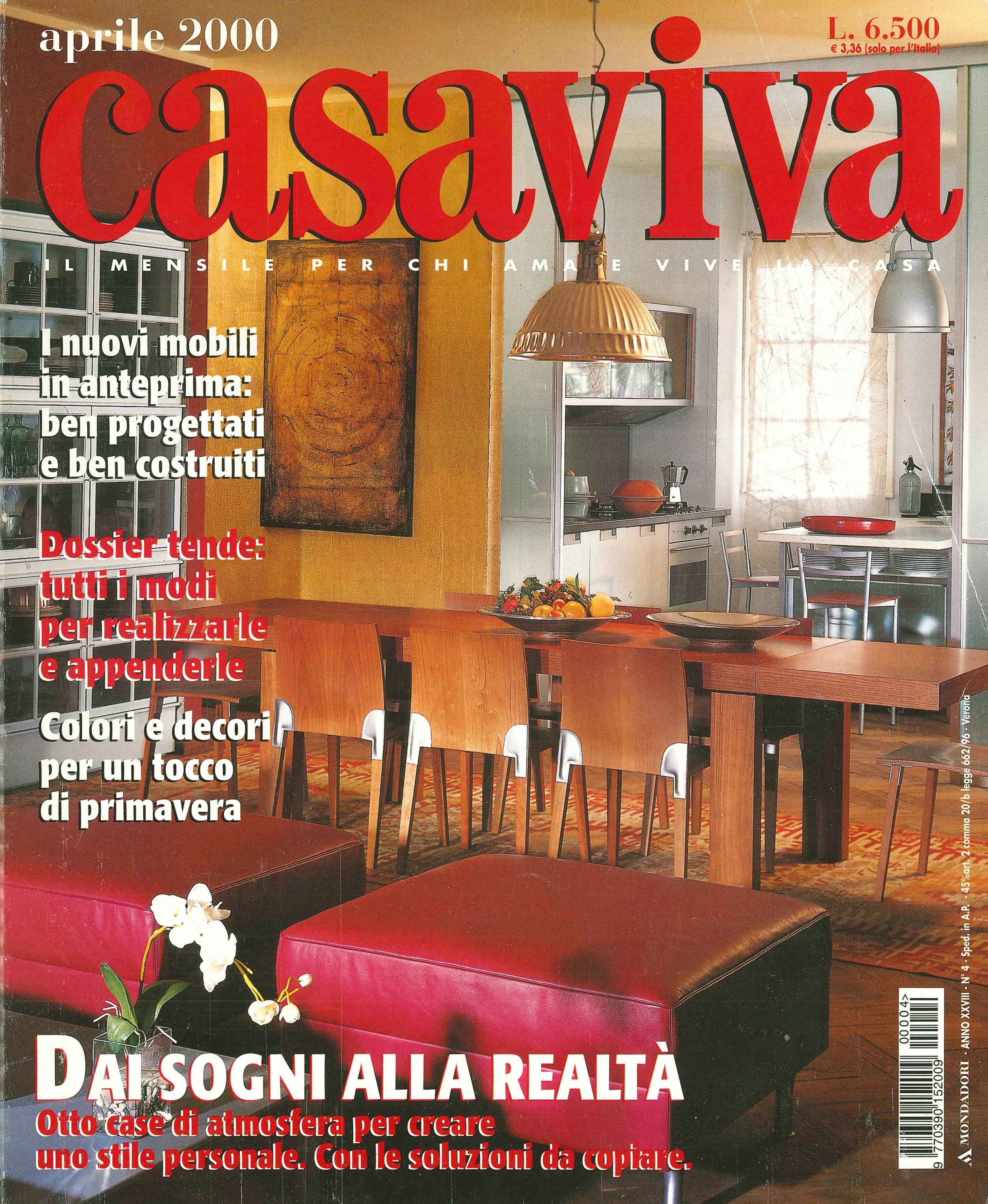 Una copertina di una rivista di interior design dal titolo 'Casaviva', aprile 2000, raffigurante un'area cucina e soggiorno con tavolo in legno, sedie e divani rossi, con luce naturale che entra da una finestra con tende leggere.