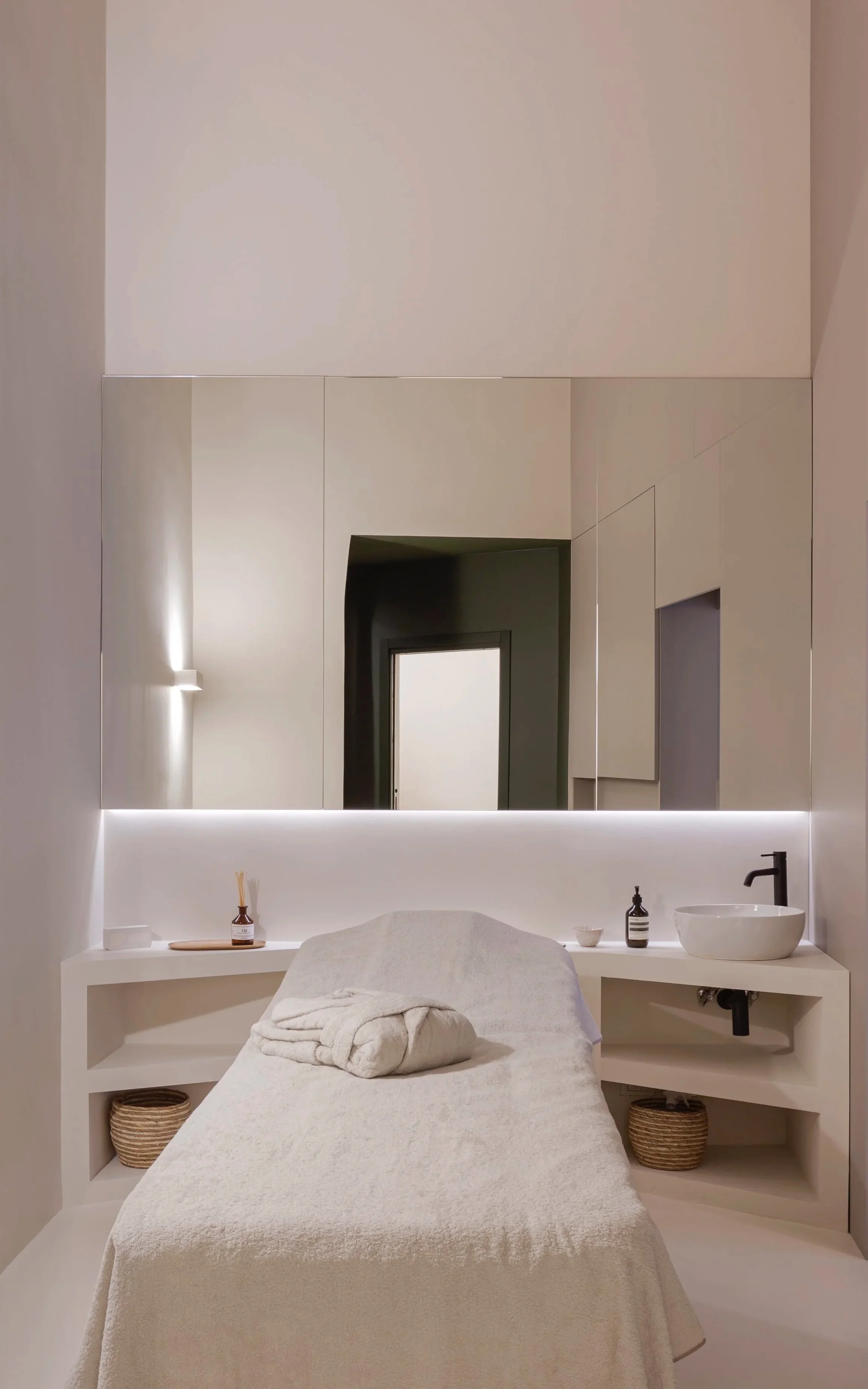 Studio di spa con letto da massaggi, grande specchio, lavabo rotondo, dispenser di sapone, biscotti, decorazioni in stile minimalista.