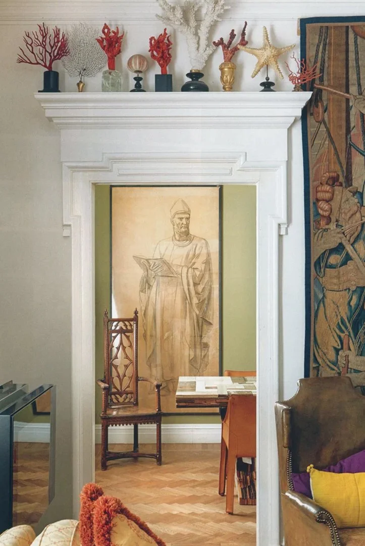 Interno con parete decorata con un dipinto di un uomo medievale, sopra una collezione di coralli e con vari arredi.