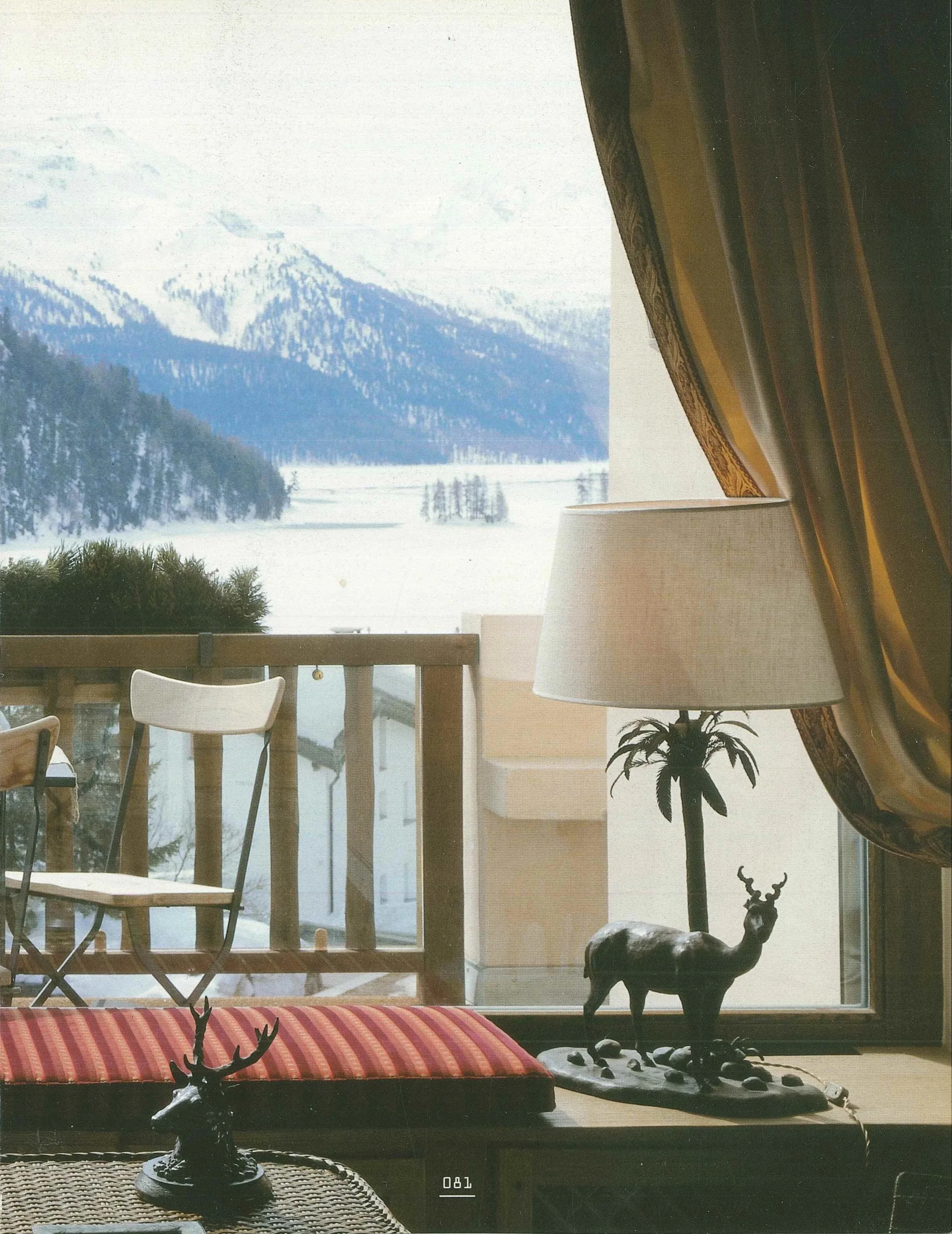 Interno con decori natalizi, lampada a terra, statuette di cervi e vista su un paesaggio innevato con montagne e laghi