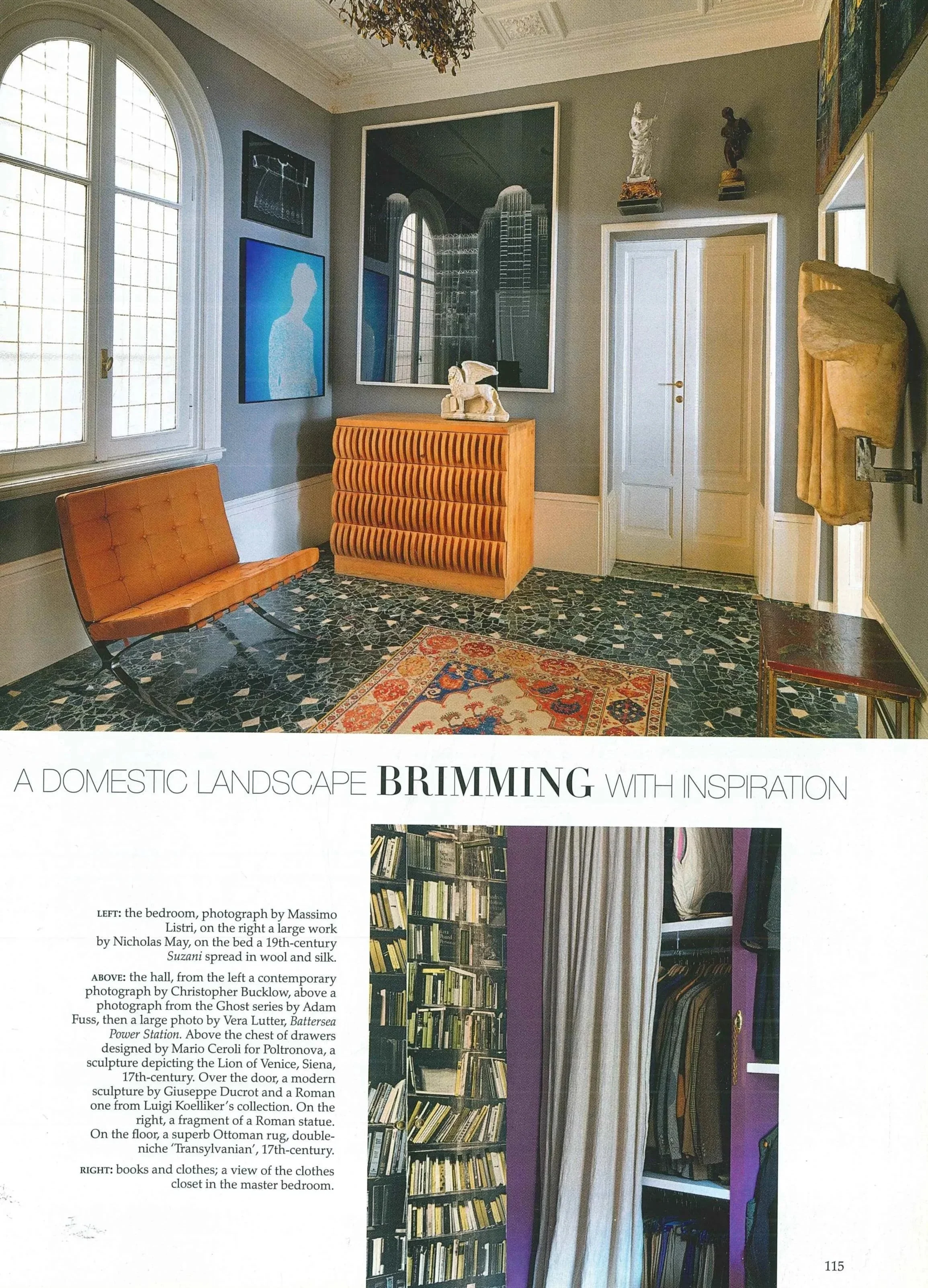 Una stanza decorata con mobili vintage, pareti dipinte di grigio con quadri moderni, una grande finestra con pannelli di vetro, un tappeto orientale e varie statue e oggetti d'arte.