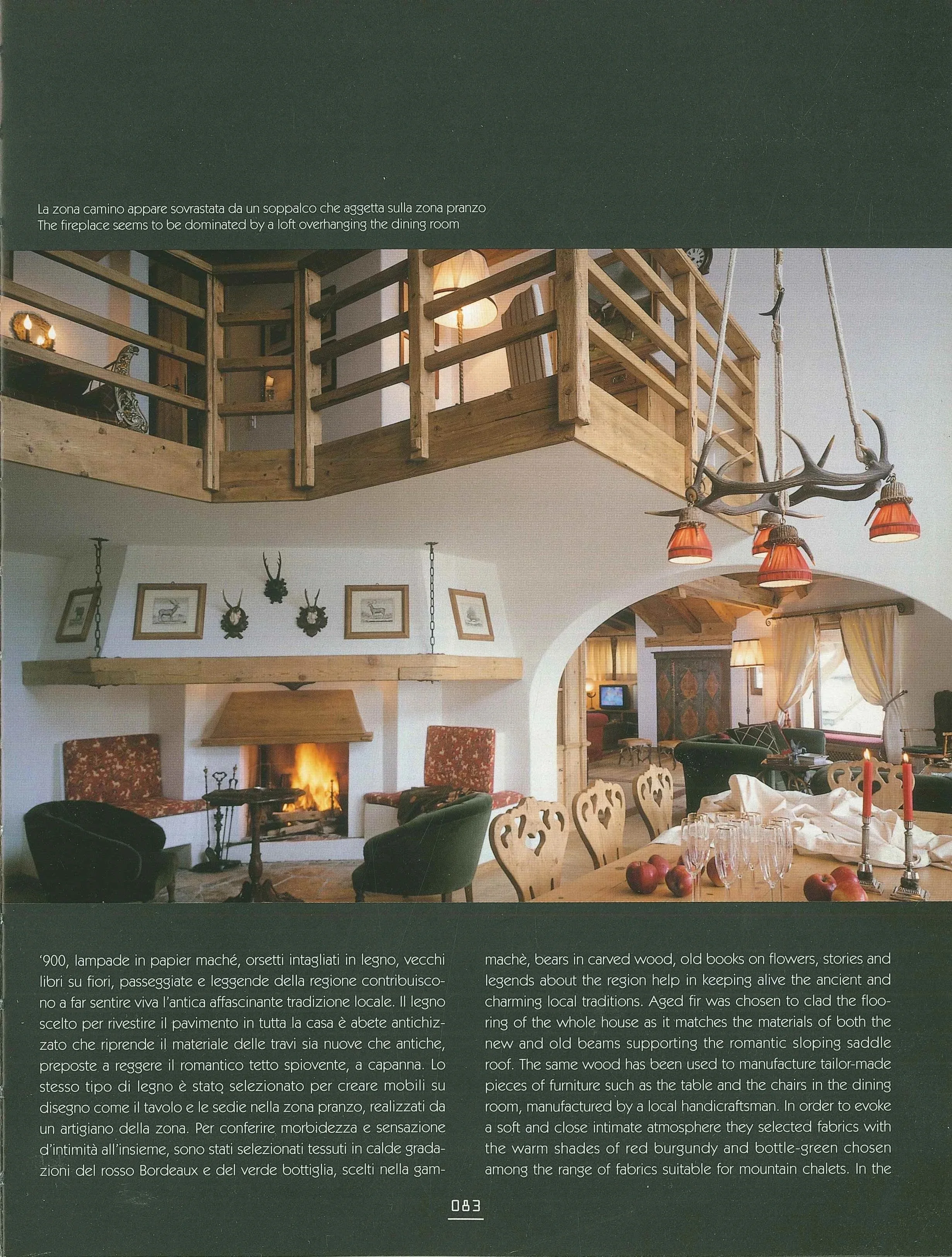 Interno di una casa con camino acceso, divani, tavolo con candeliere, e una cucina in stile rustico. La stanza ha decorazioni di cervi e libri antichi, con una zona soppalcata sopra il camino.