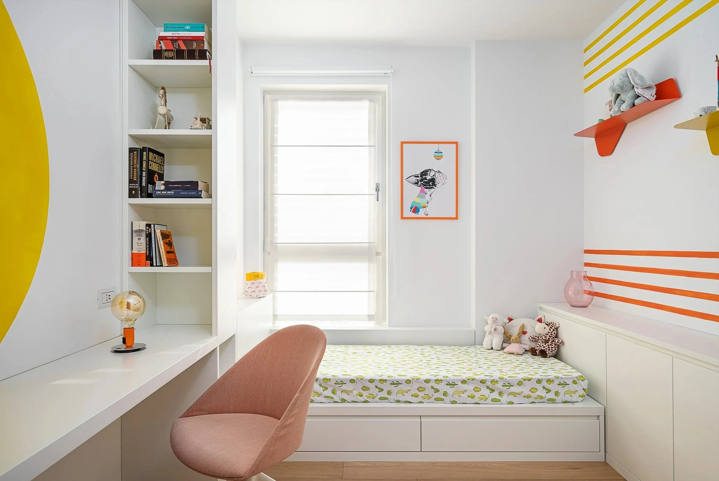 Camera per bambini con letto, scrivania, scaffali con libri e decorazioni colorate, vestiti e pupazzi, luce naturale da finestra.