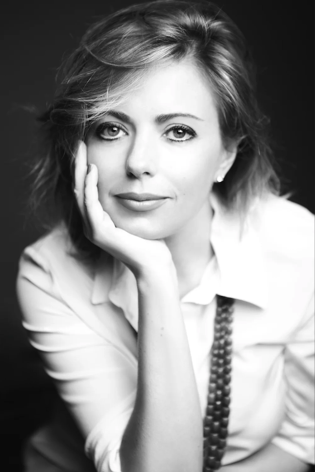 Ritratto in bianco e nero di una donna con capelli corti, che sorride leggermente, con il mento appoggiato sulla mano.