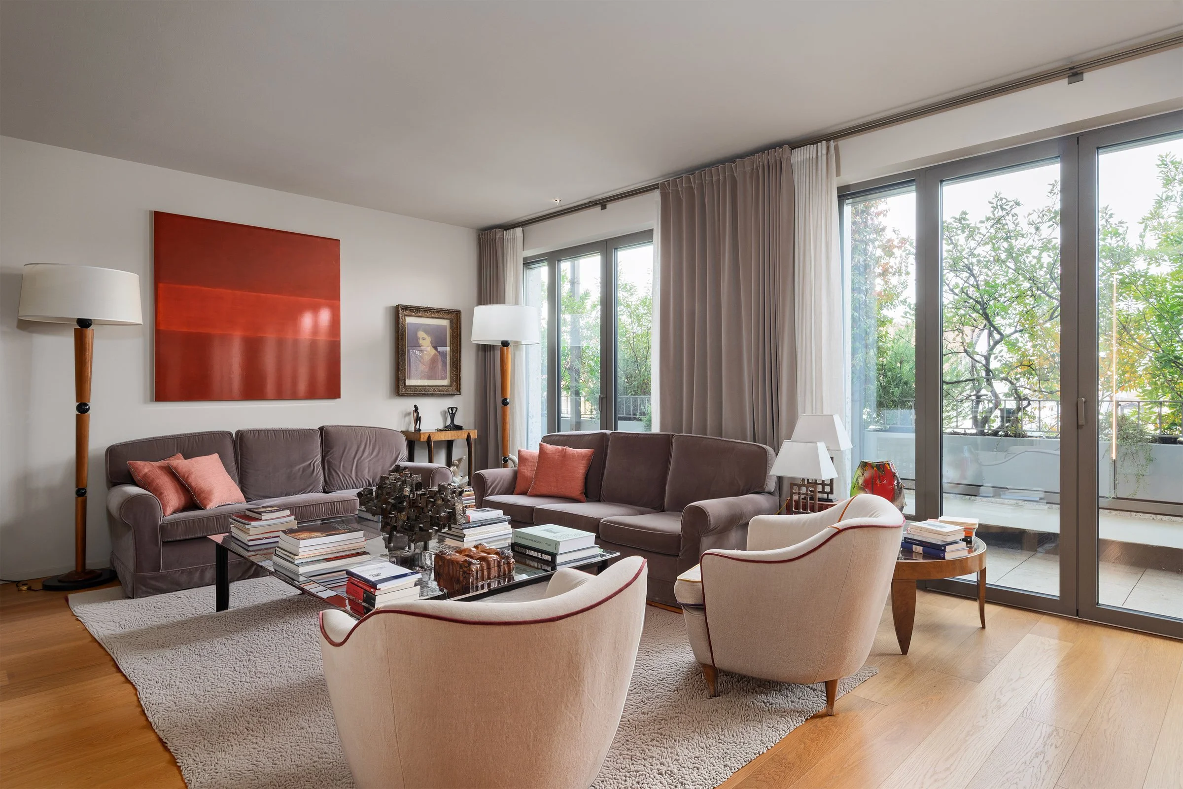 Soggiorno elegante con divani, poltrone, tavolini, lampade e decorazioni, balcone con vista su alberi
