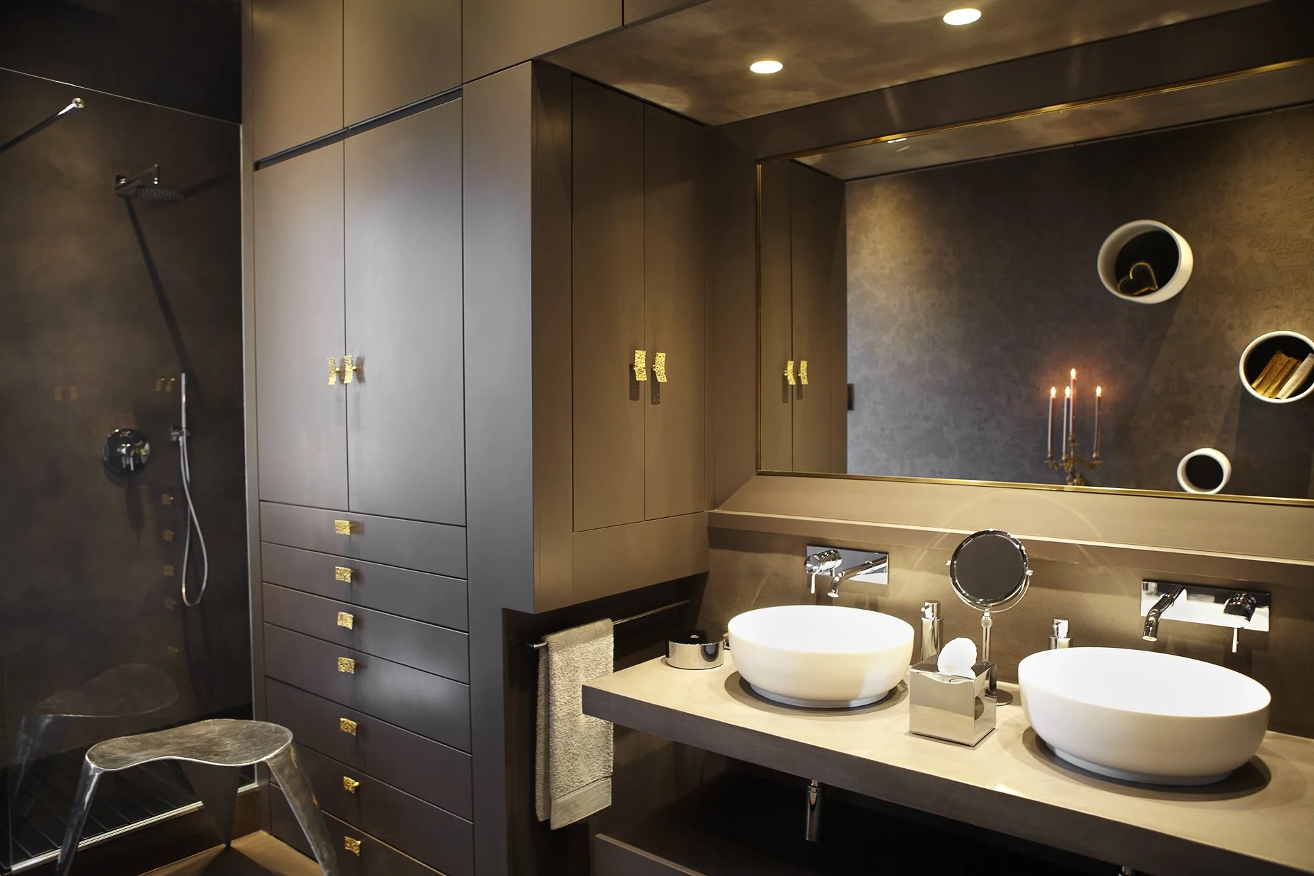 Bagno moderno con doppio lavabo, grande specchio, armadietti laccati, lampada ad asta, mobili in tonalità marrone, scaffali circolari con libri e decorazioni, soffitto illuminato, lavandino rotondo e accessori di design.
