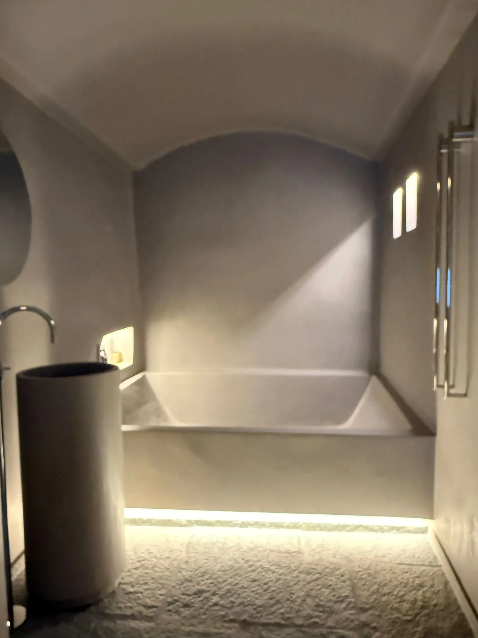 Interno di una vasca da bagno moderna con pareti e pavimenti chiari, illuminata da luci soffuse