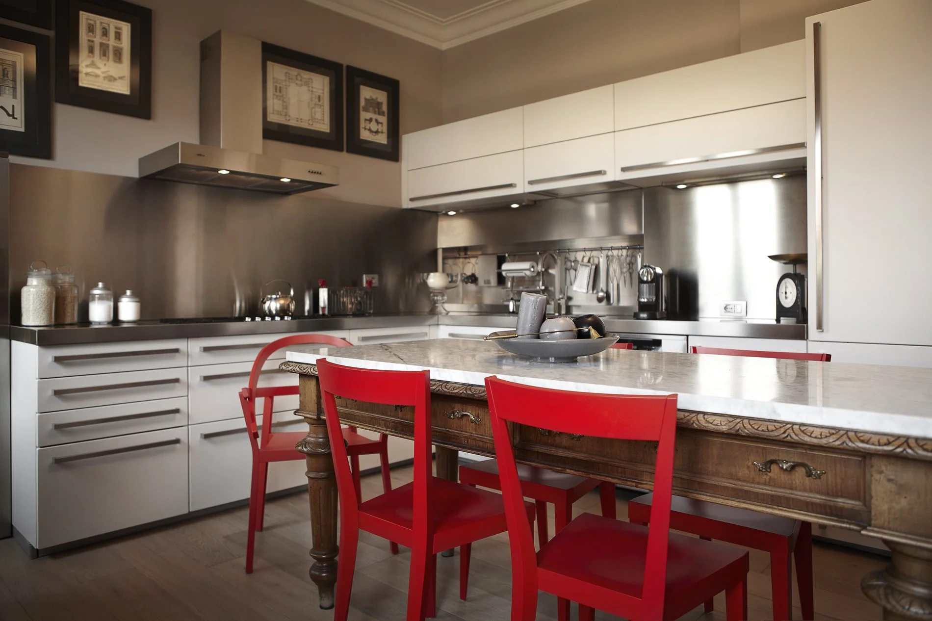 Cucina moderna con piano di lavoro in marmo, sedie rosse e mobili bianchi.