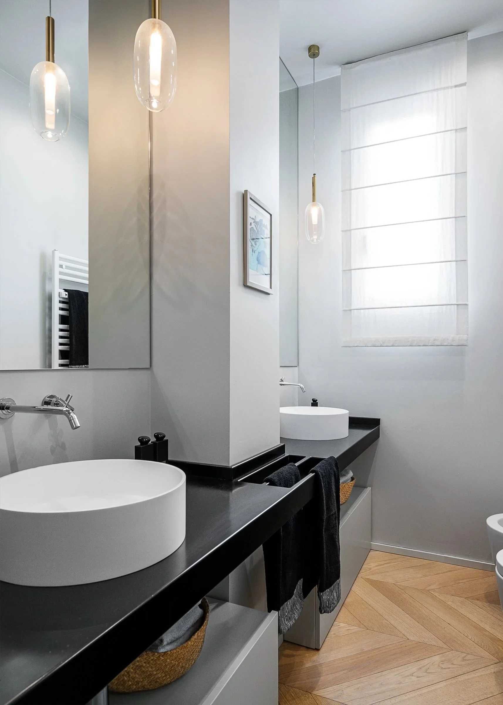 Bagno moderno con due lavandini rotondi bianchi, specchi grandi, illuminazione a pendente e finestra con tende bianche.