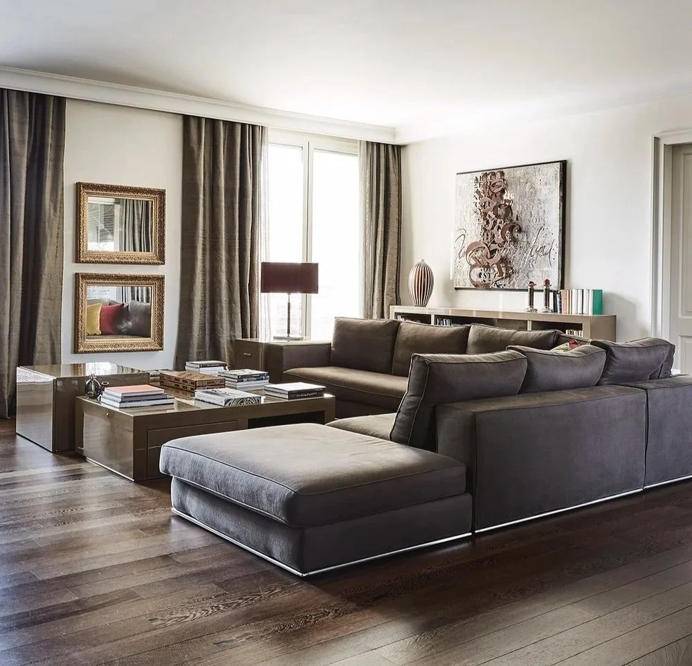 Salotto con divani grigi, tavolino, quadri alle pareti, lampada da tavolo, parete bianca, tappeto in legno scuro.