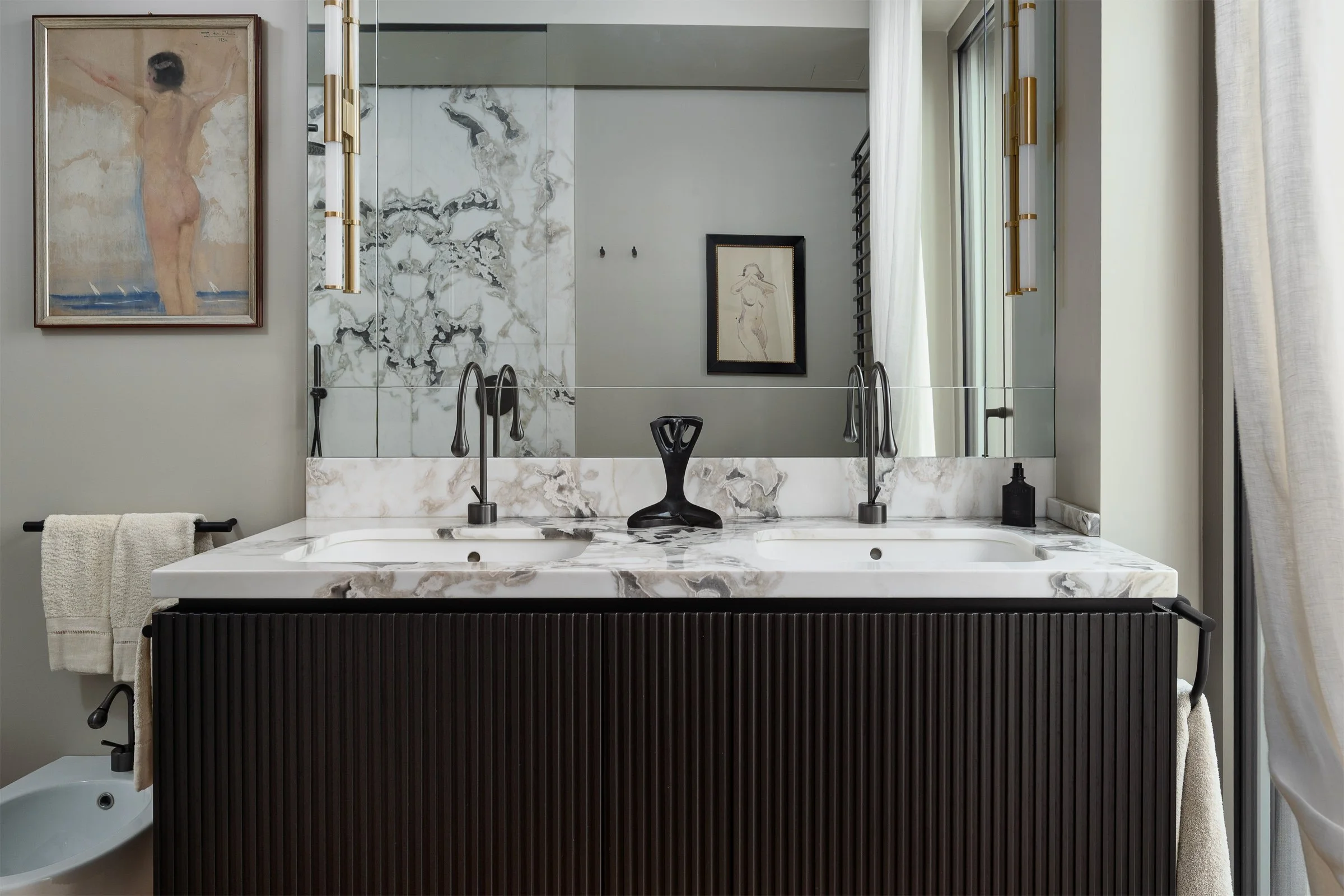 Un lavabo doppio con piano in marmo e specchio grande con cornice. Decorazioni artistiche e tende leggere nel bagno elegante.