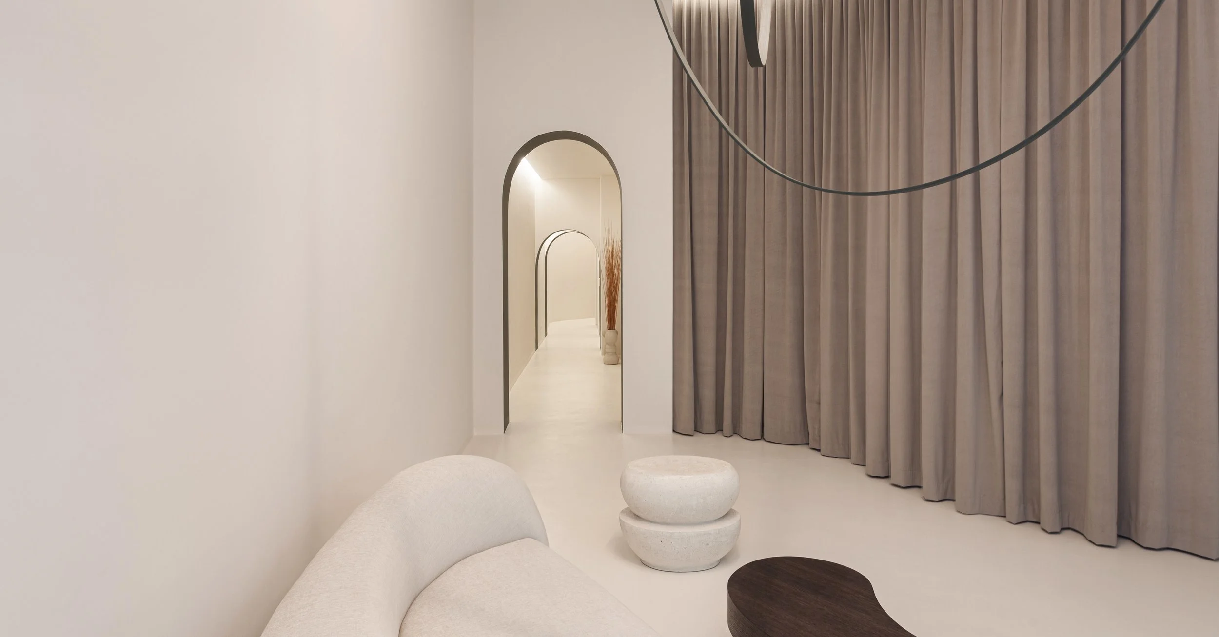 Interno minimalista con divano bianco e tende beige, nel mirino un'arcata che conduce a un corridoio decorato con vasi e un ramo di fiori secchi.