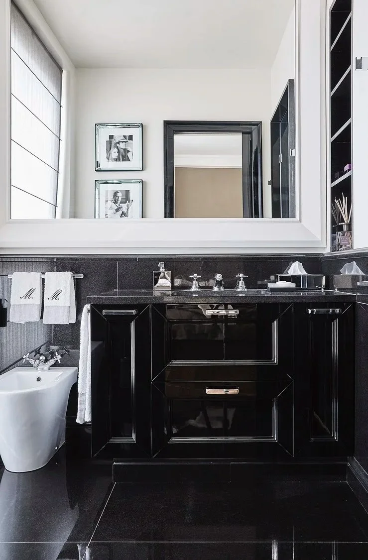 Un bagno elegante con lavabo nero, specchio grande, bidet bianco, asciugamani personalizzati, arredi moderni e decorazioni monocromatiche.