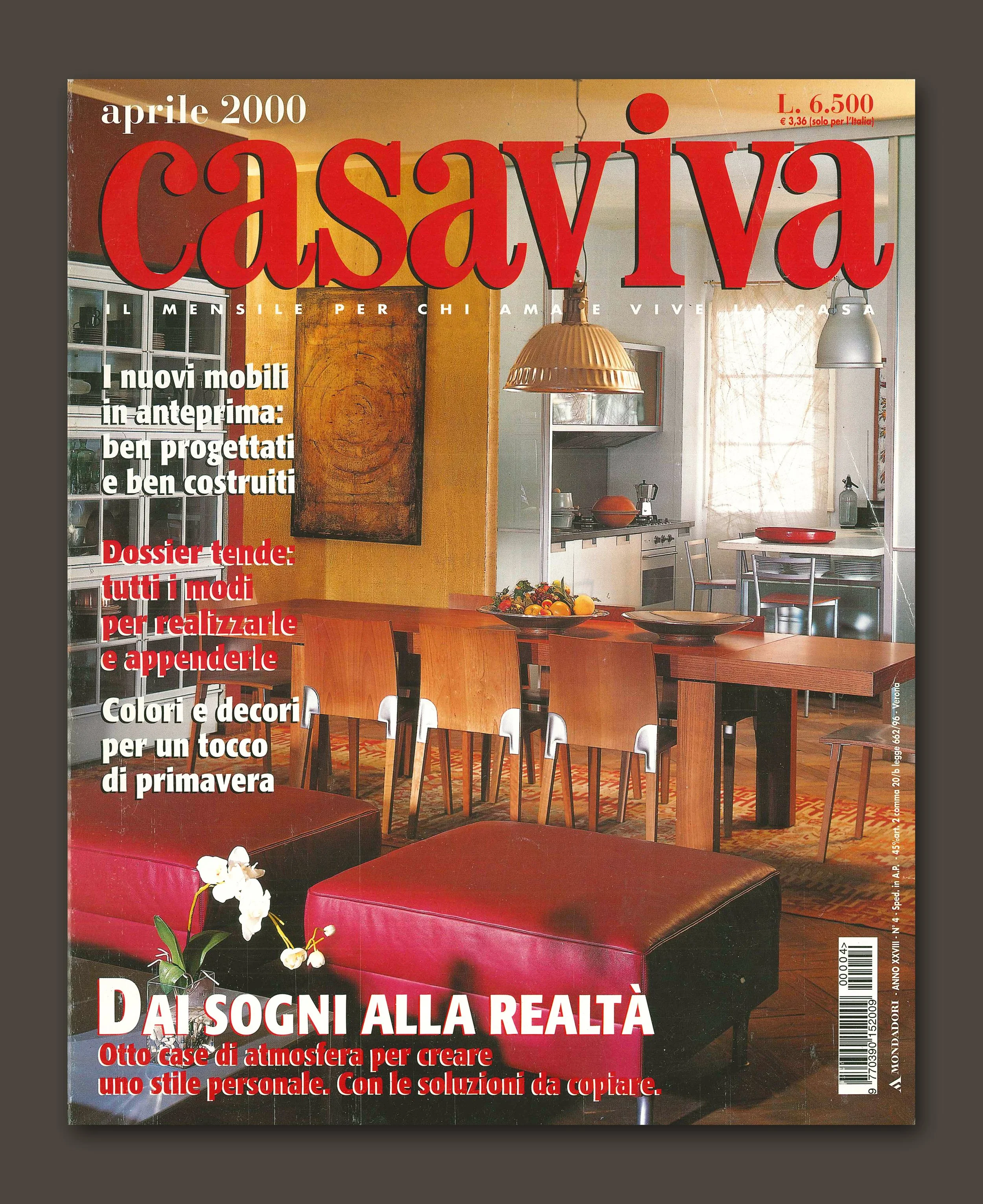 Copertina di una rivista intitolata 'Casaviva' con un'immagine di un interno domestico con tavolo in legno, sedie e illuminazione moderna, decorazioni e una finestra con tende leggere.