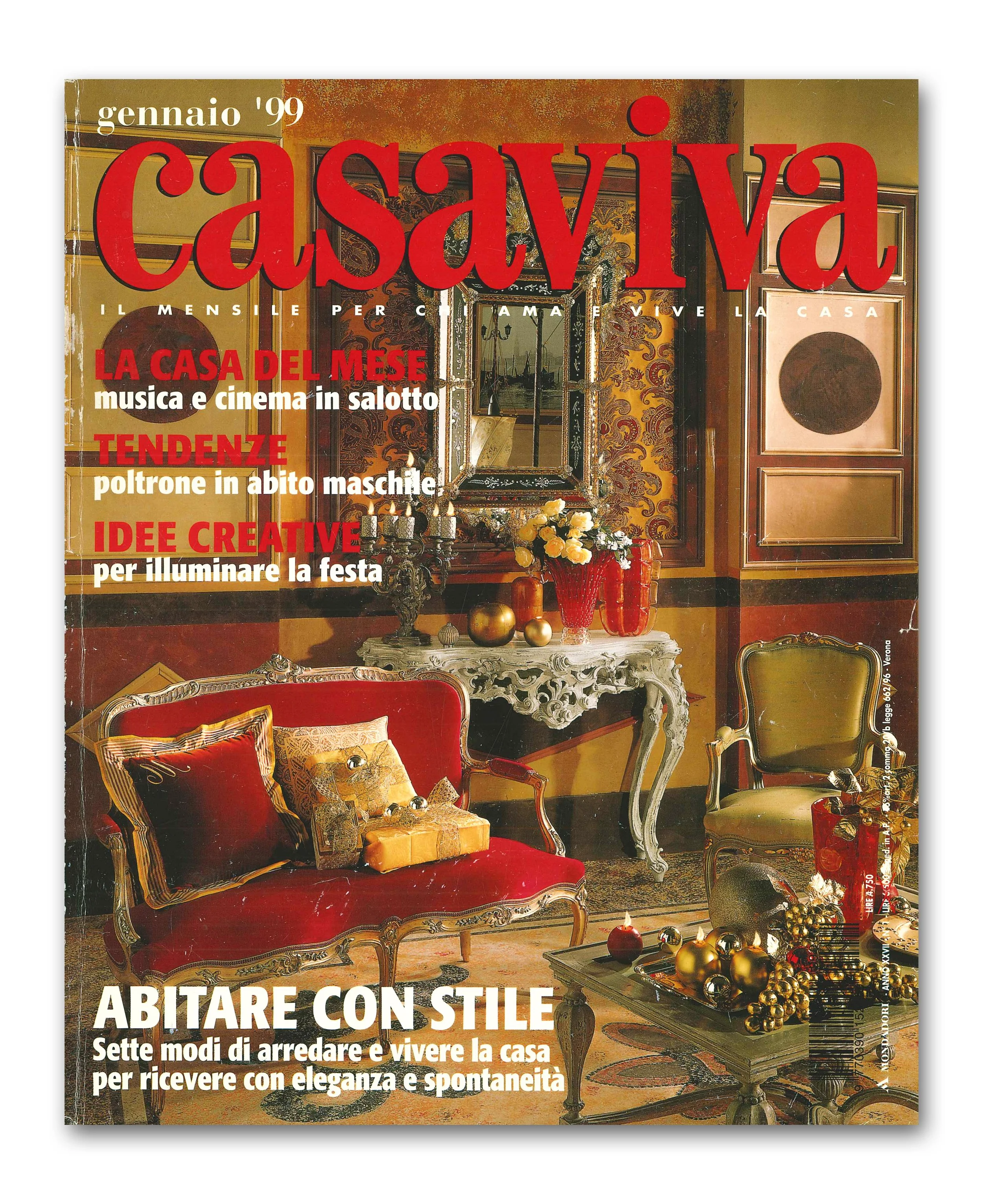 Copertina di rivista con arredamento elegante e tradizionale, divano rosso con cuscini, tavolino decorato con ornamenti dorati e vasi di fiori, pareti con quadri e specchio.
