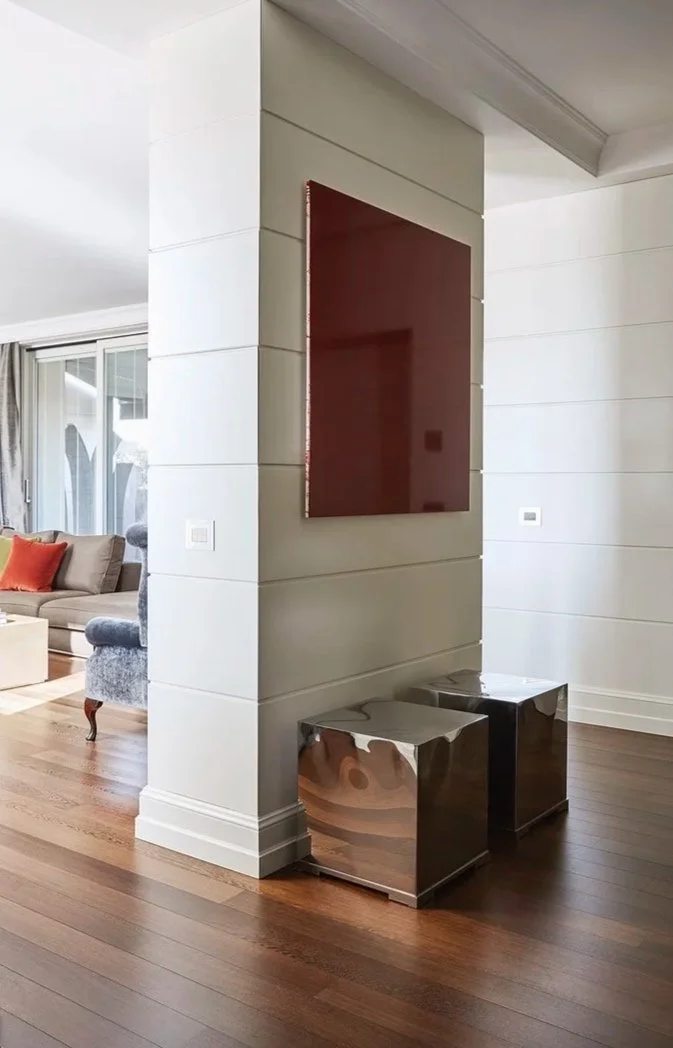 Angolo di un soggiorno con pareti bianche, un quadro rosso, due mobili metallici argentati e un soggiorno con divano beige e cuscini arancioni, cose vicine alla parete di ingresso.