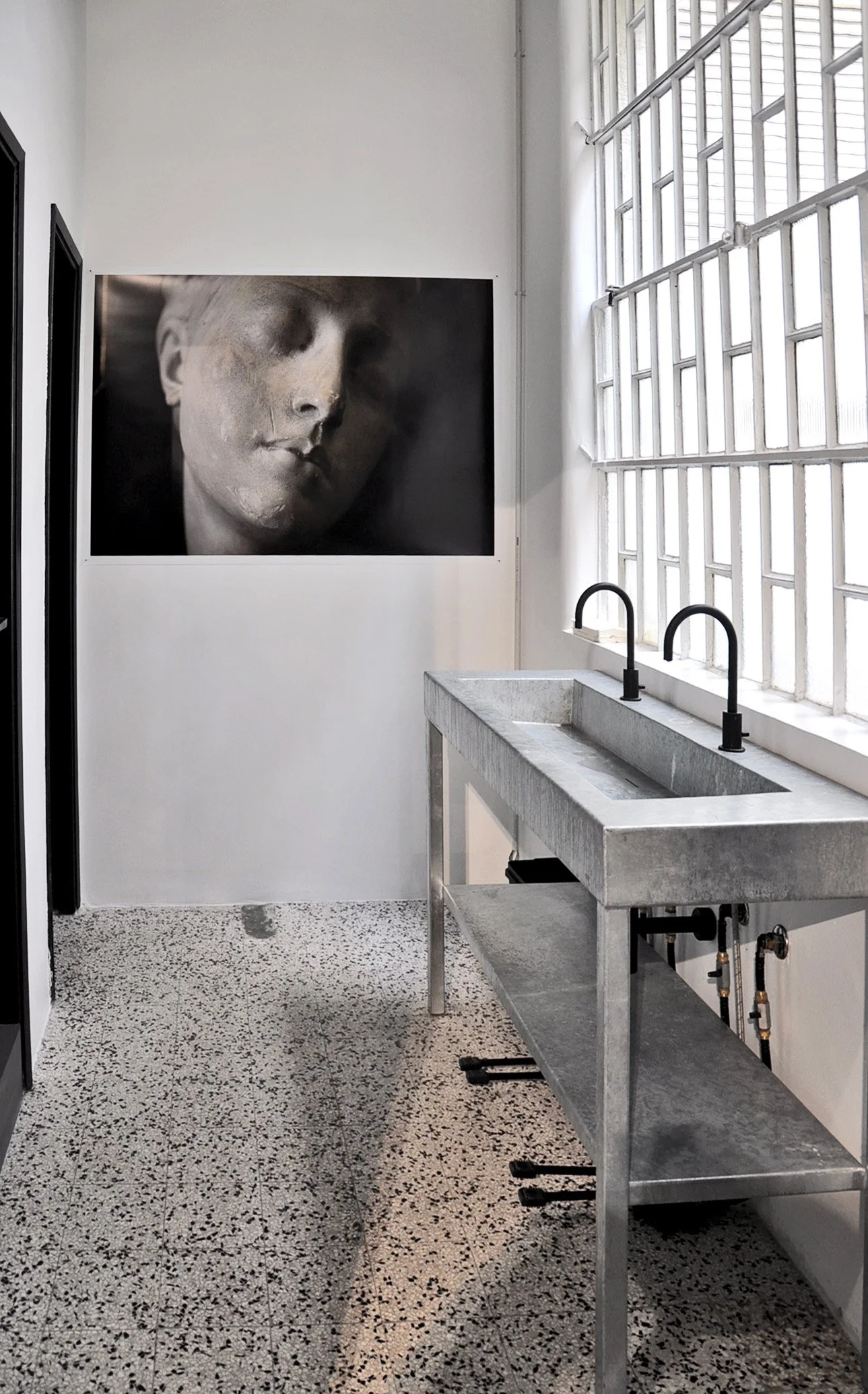 Interno con grande finestra di vetro, lavandino in cemento e un dipinto di una statua di un volto umano femminile