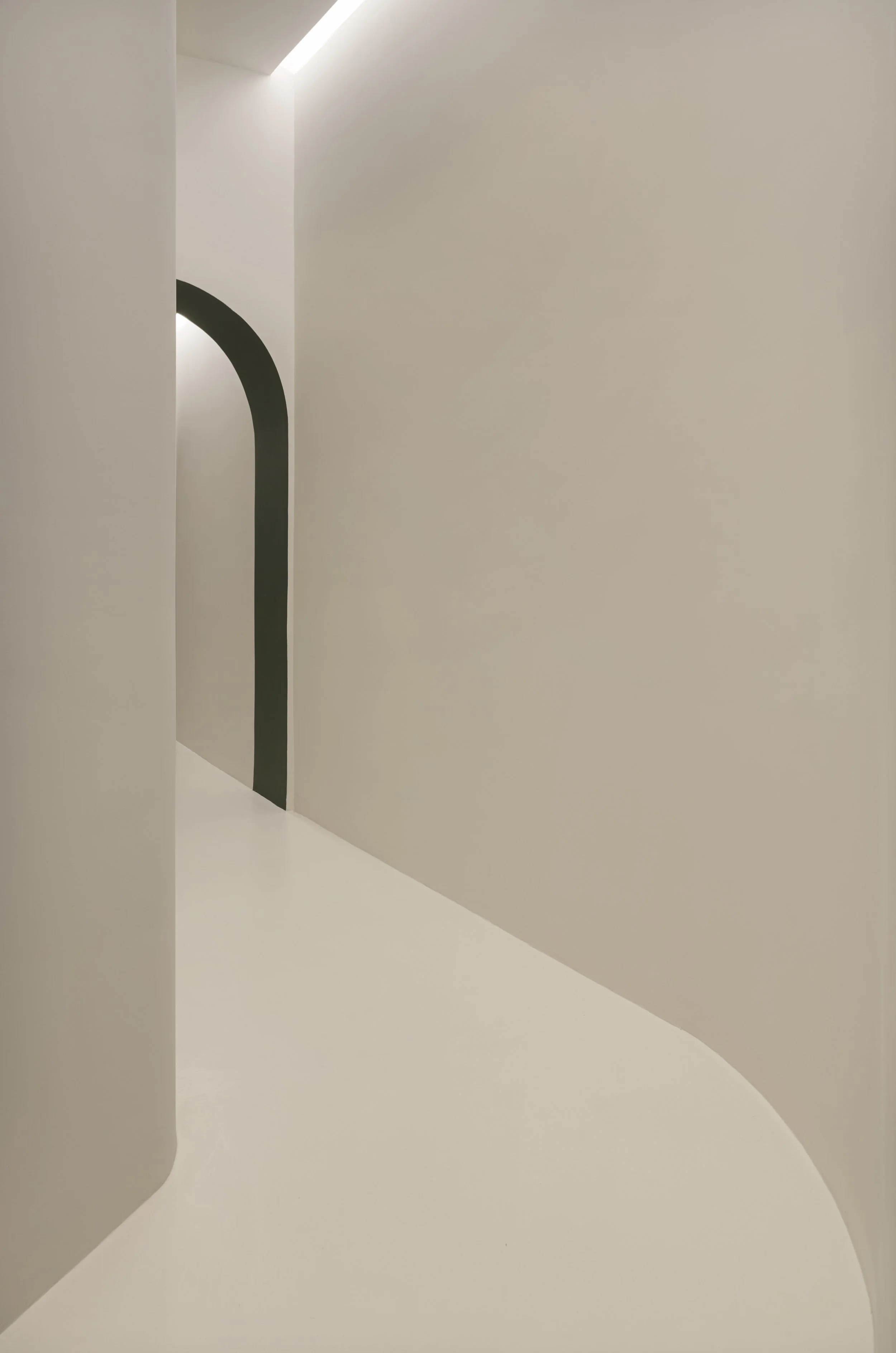 Interno minimalista con pareti bianche, un portale ad arco nero e illuminazione soffusa.