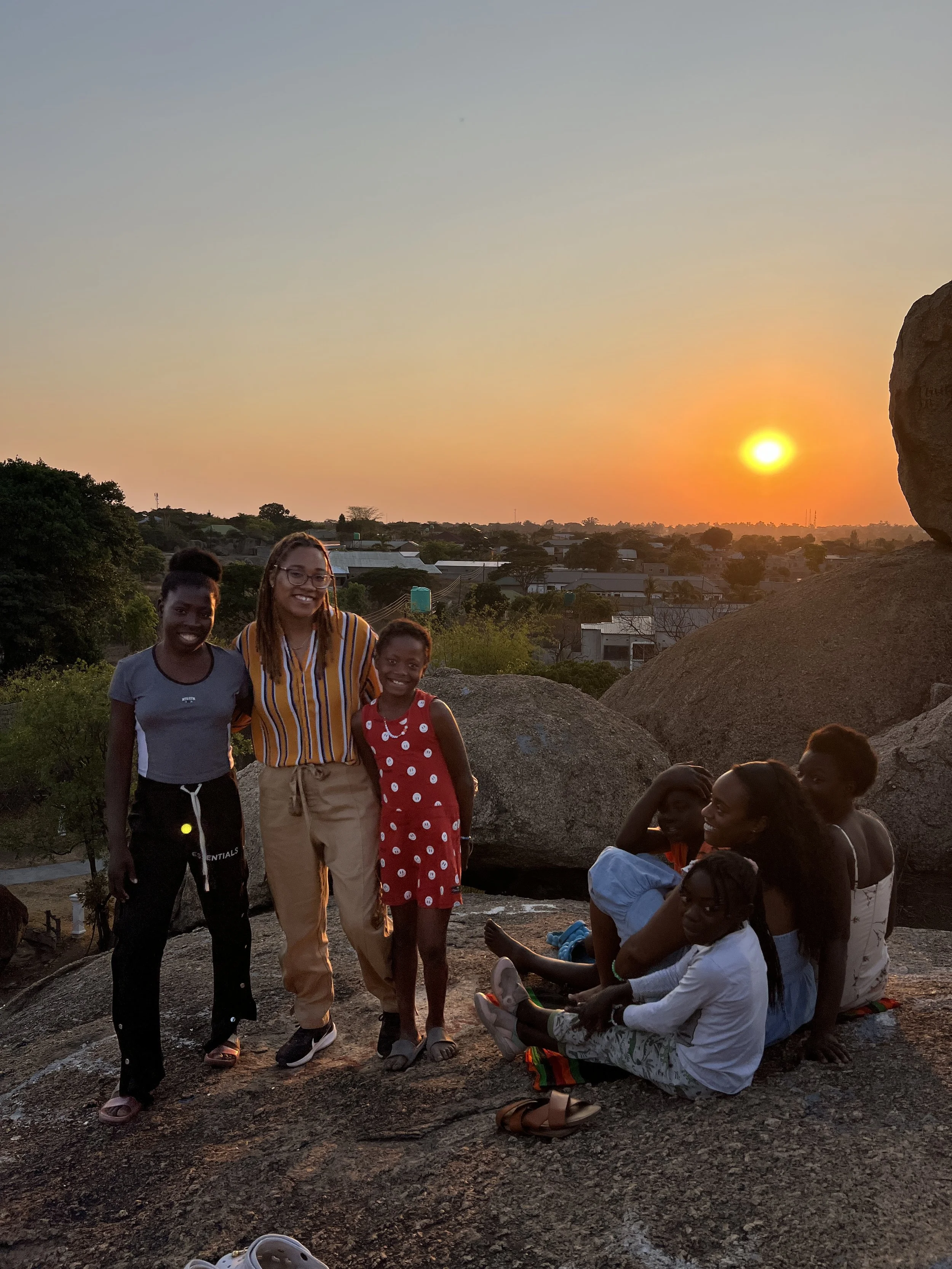 Group of children and a woman enjoying sunset on rocky terrain in a residential area.