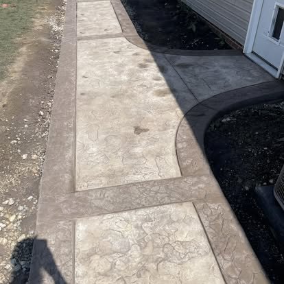 Concrete sidewalk with decorative stamped design next to a house and garden bed.