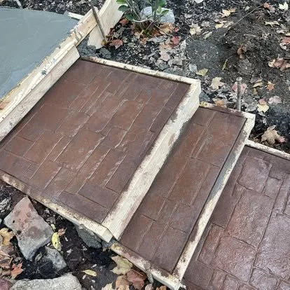 Three rectangular stepping stones with brick patterns in a garden bed, surrounded by soil and fallen leaves.