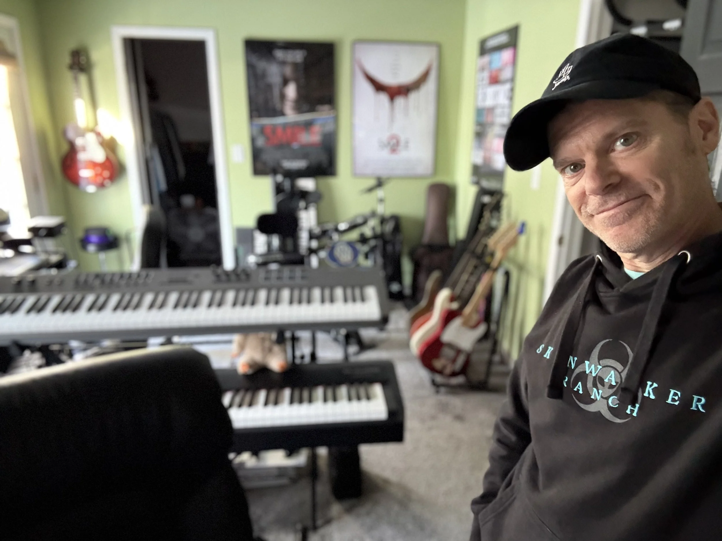 Man taking a selfie in a music studio with guitars and keyboards in the background.