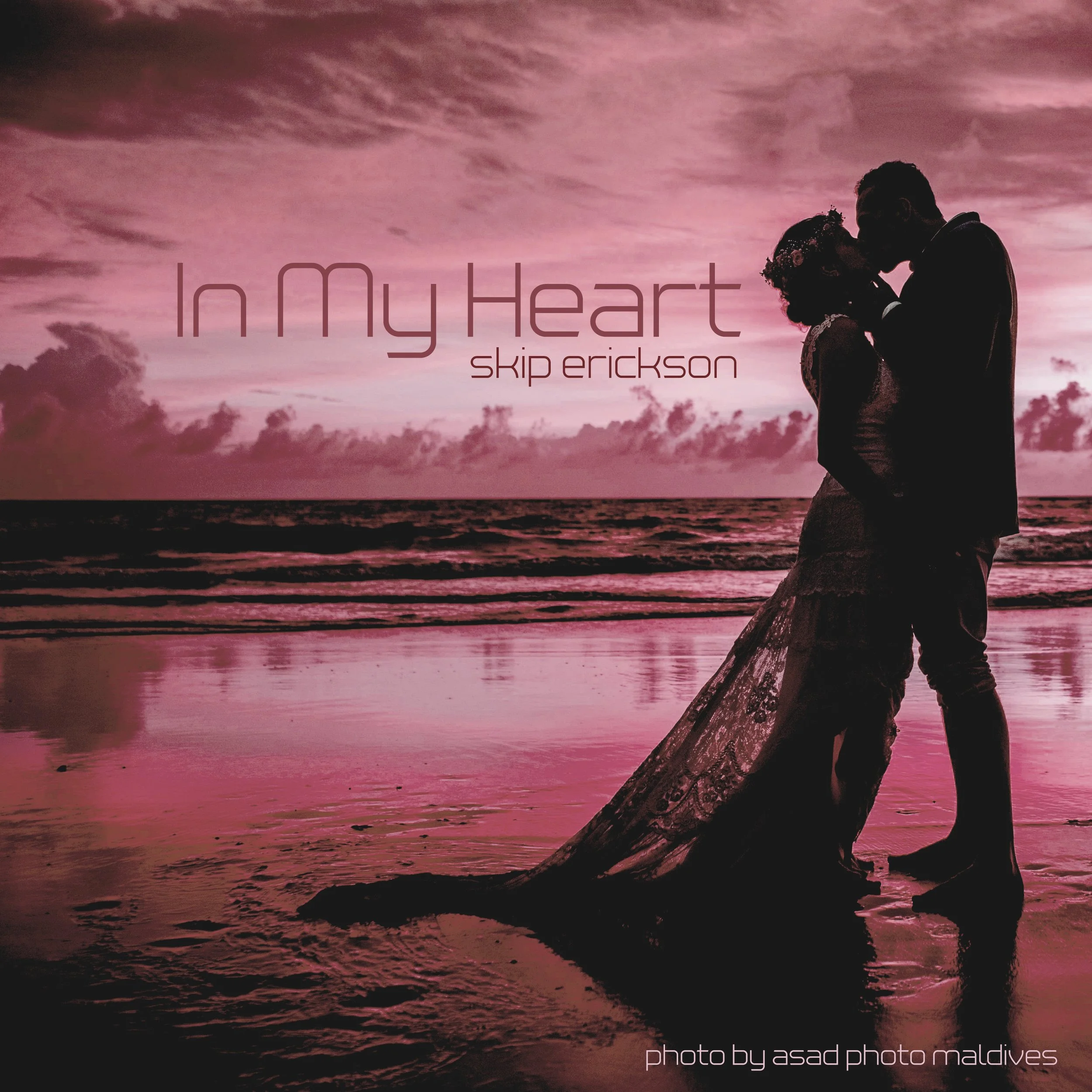 Silhouette of a couple kissing on a beach at sunset with pink sky and ocean in the background, text overlay reads 'In My Heart by Skip Erickson', and at the bottom, 'photo by Asad Photo Maldives'.